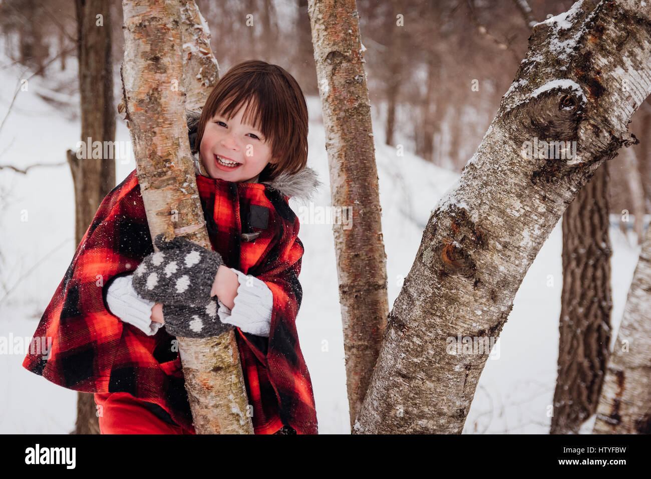 Girl in hooded parka standing amongst trees in winter Stock Photo