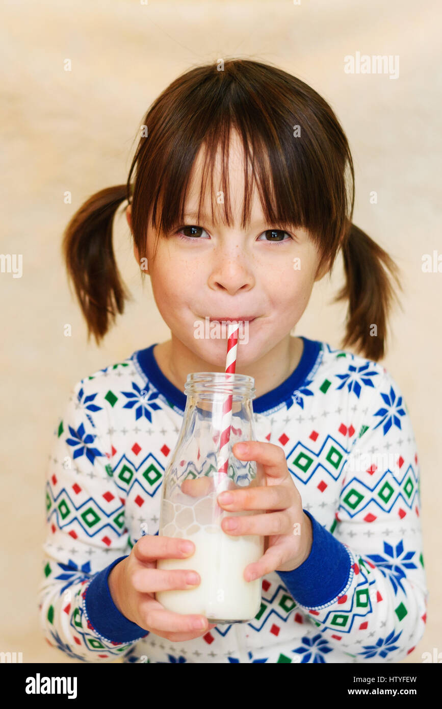 Girl in pyjamas drinking bottle of milk with a drinking straw Stock Photo