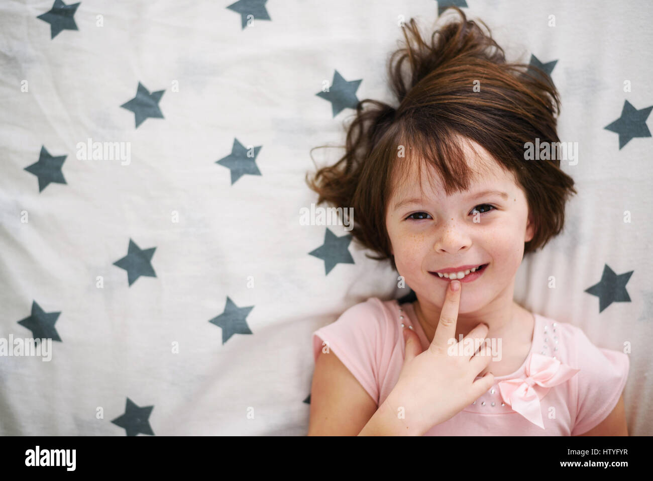 Overhead view of smiling girl lying in bed with finger on her lips Stock Photo