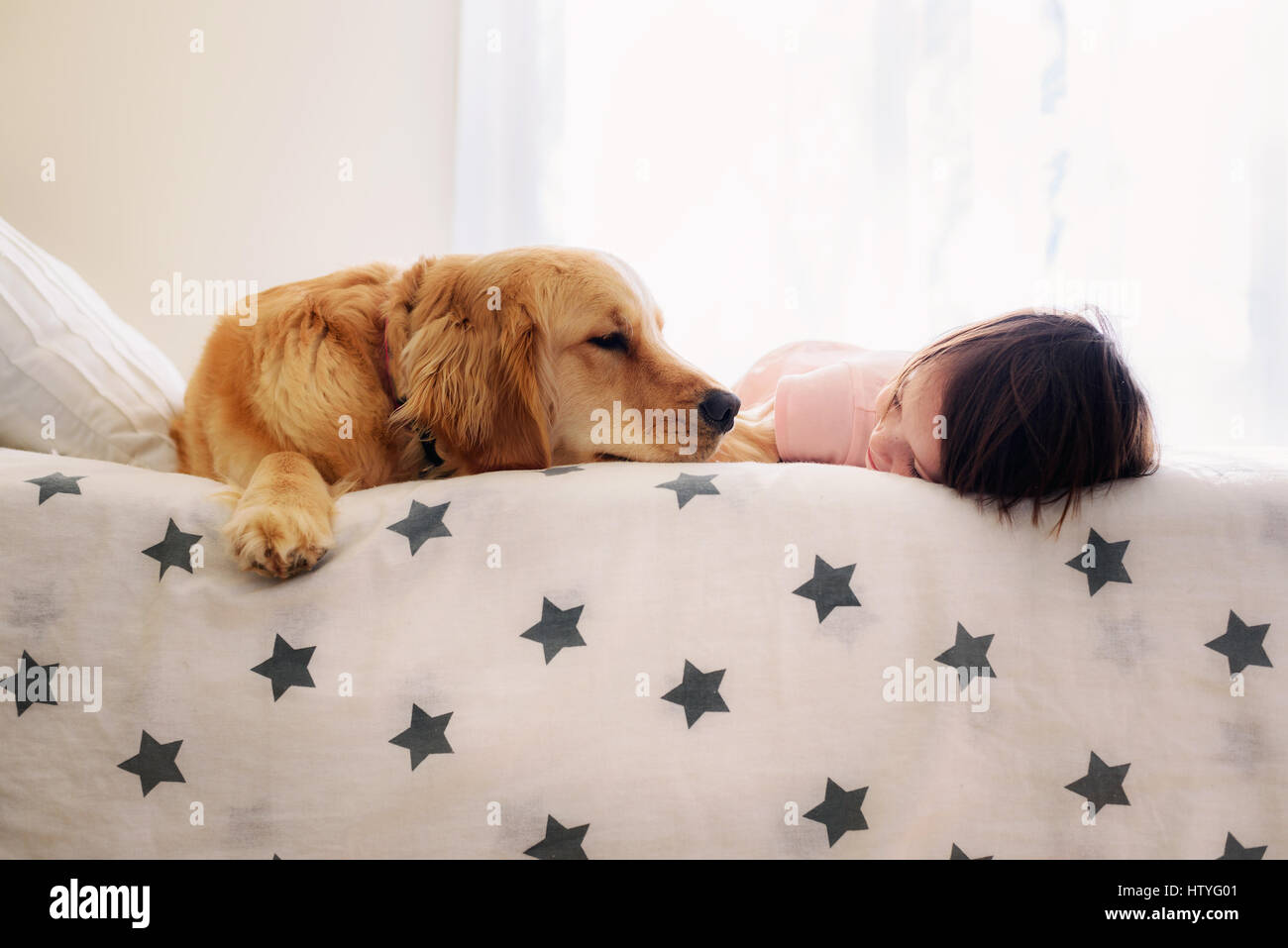 Smiling Girl lying on a bed next to a golden retriever dog Stock Photo