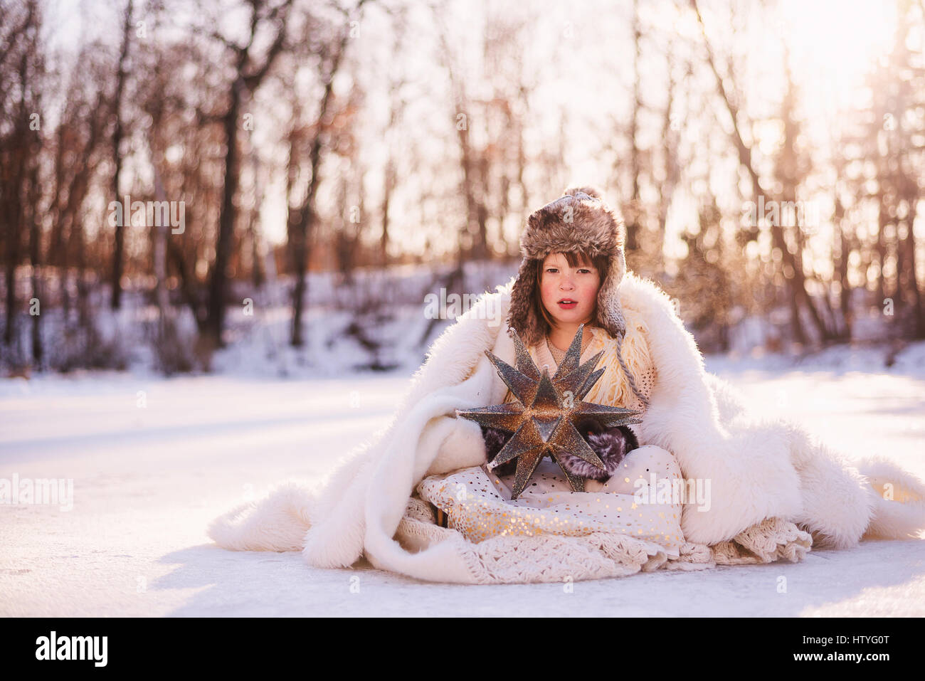 Girl dressed as snow queen sitting in the snow Stock Photo