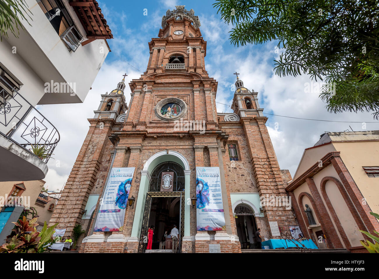 Looking up at the Puerto Vallarta church Our Lady of Guadalupe from close up with wide angle lens and full corners, lady in red standing in  doorway. Stock Photo