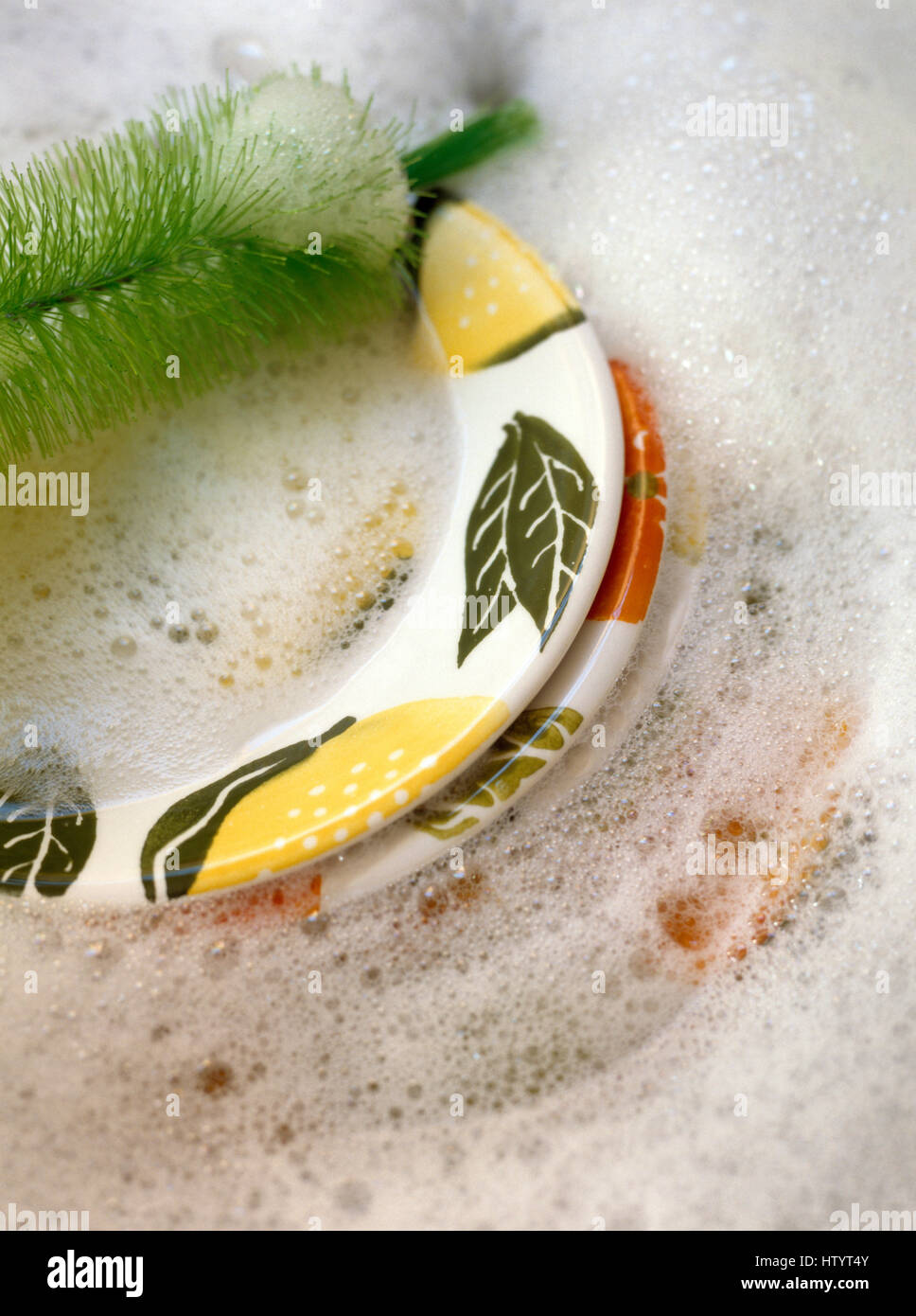 Close-up of hand painted plates in a washing up bowl with soap suds and a green washing up brush Stock Photo