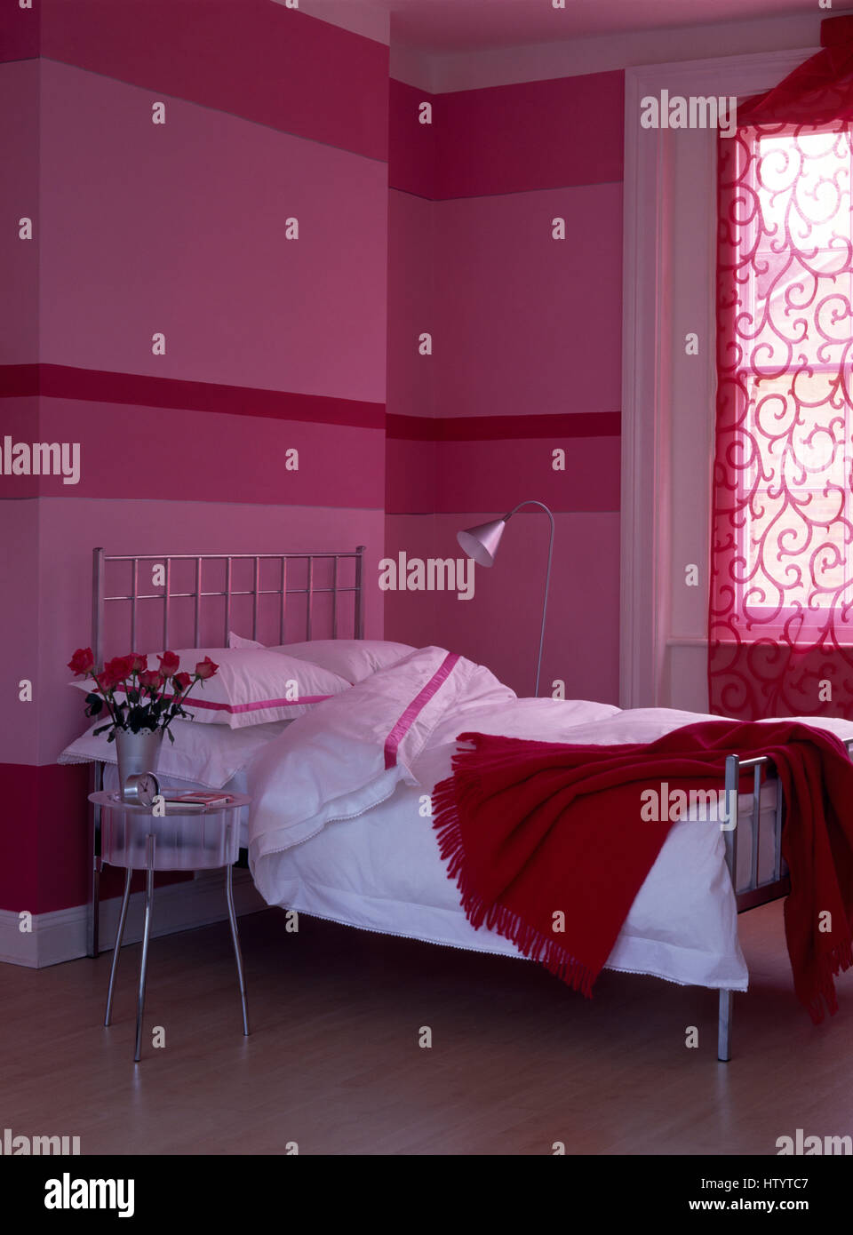Wall painted in horizontal stripes in a pink economy style bedroom with a  red wool throw and white bedlinen on the bed Stock Photo - Alamy