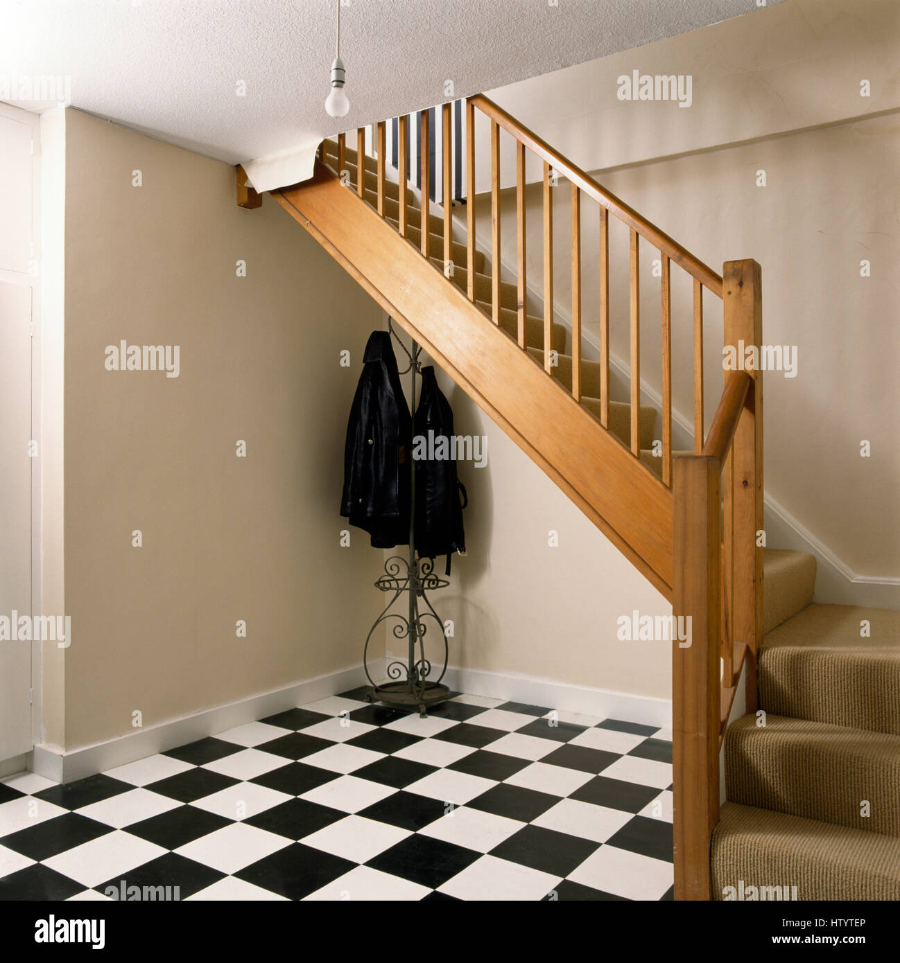 Black+white chequerboard floor in hall with wooden staircase and a simple coat stand Stock Photo
