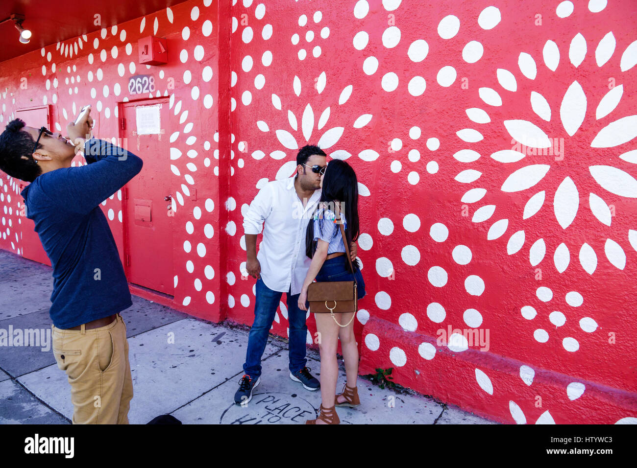 Miami Florida,Wynwood,urban graffiti,street art,painted wall mural,Hispanic woman female women,man men male,couple,kissing,picture,smartphone cell pho Stock Photo