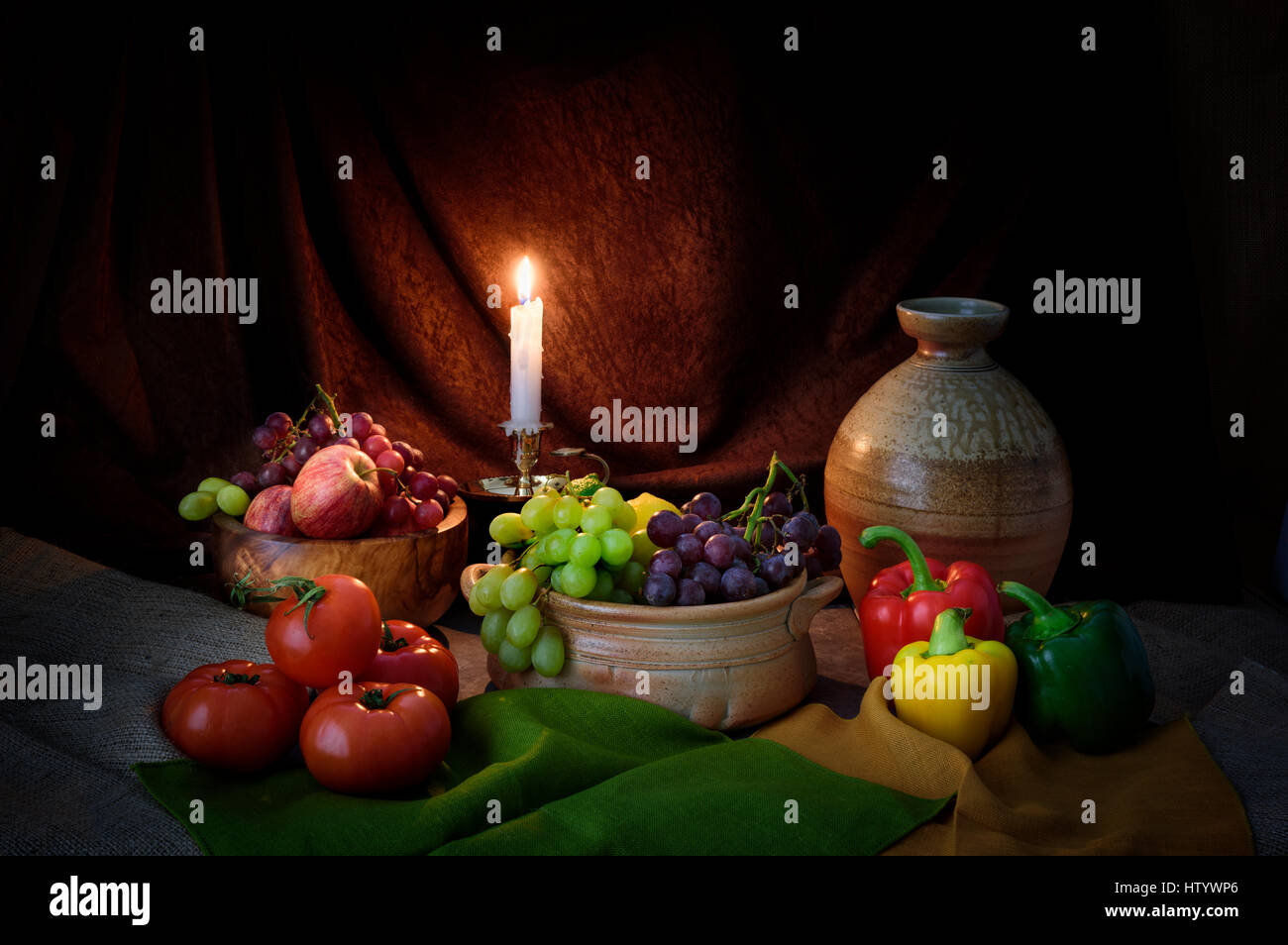 Candle lit still life photograph of fruit and vegetables in style of old master  of apples tomatoes grapes candle light and rustic pottery Stock Photo