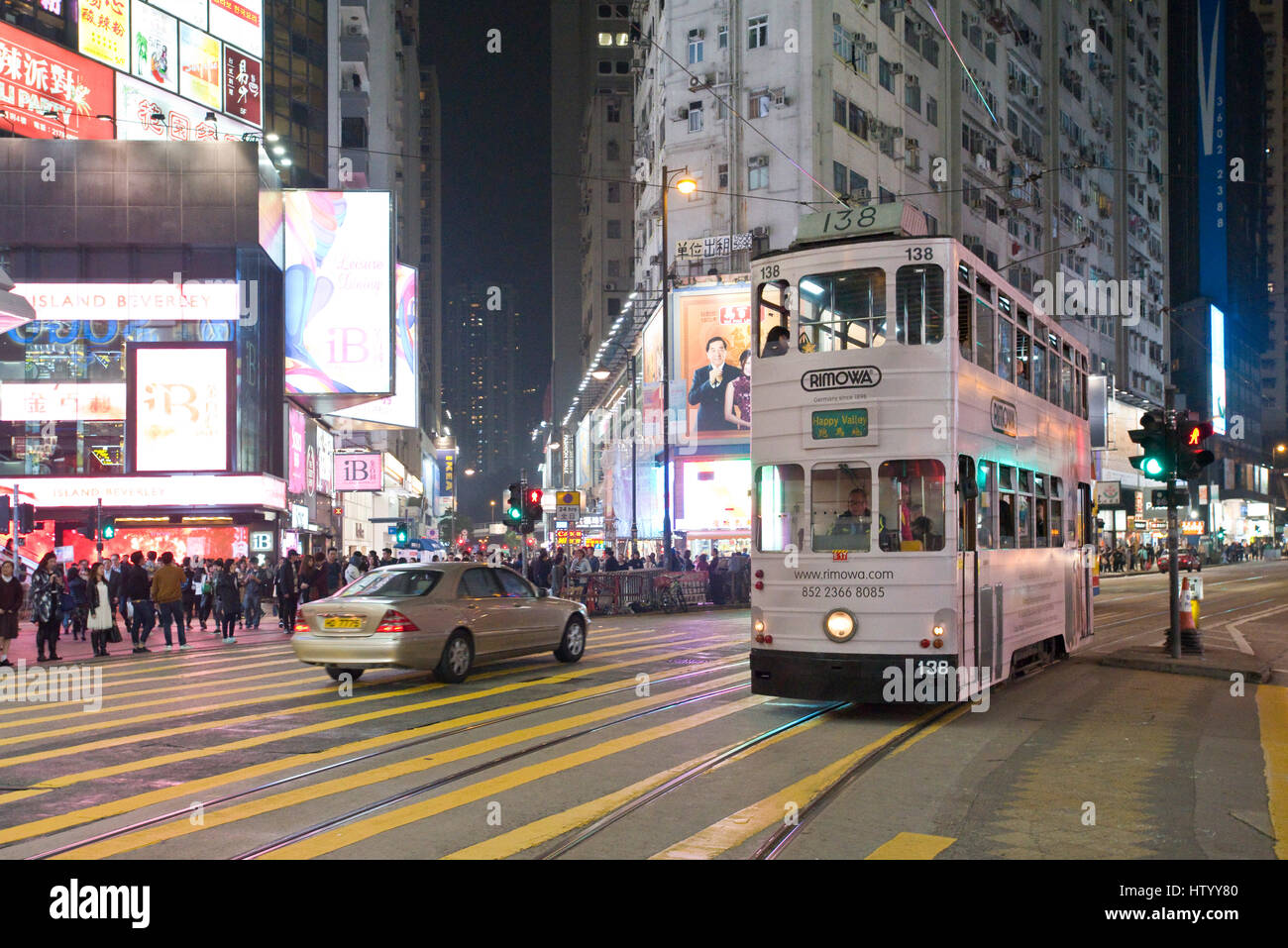 A tram crossing a busy intersection for pedestrians crossing the street with neon lights in Causeway Bay, Hong Kong Island, with some motion blur. Stock Photo