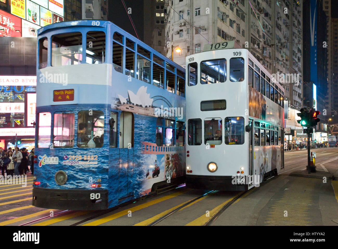 2 trams crossing a busy intersection for pedestrians crossing the street with neon lights in Causeway Bay, Hong Kong Island, with some motion blur. Stock Photo