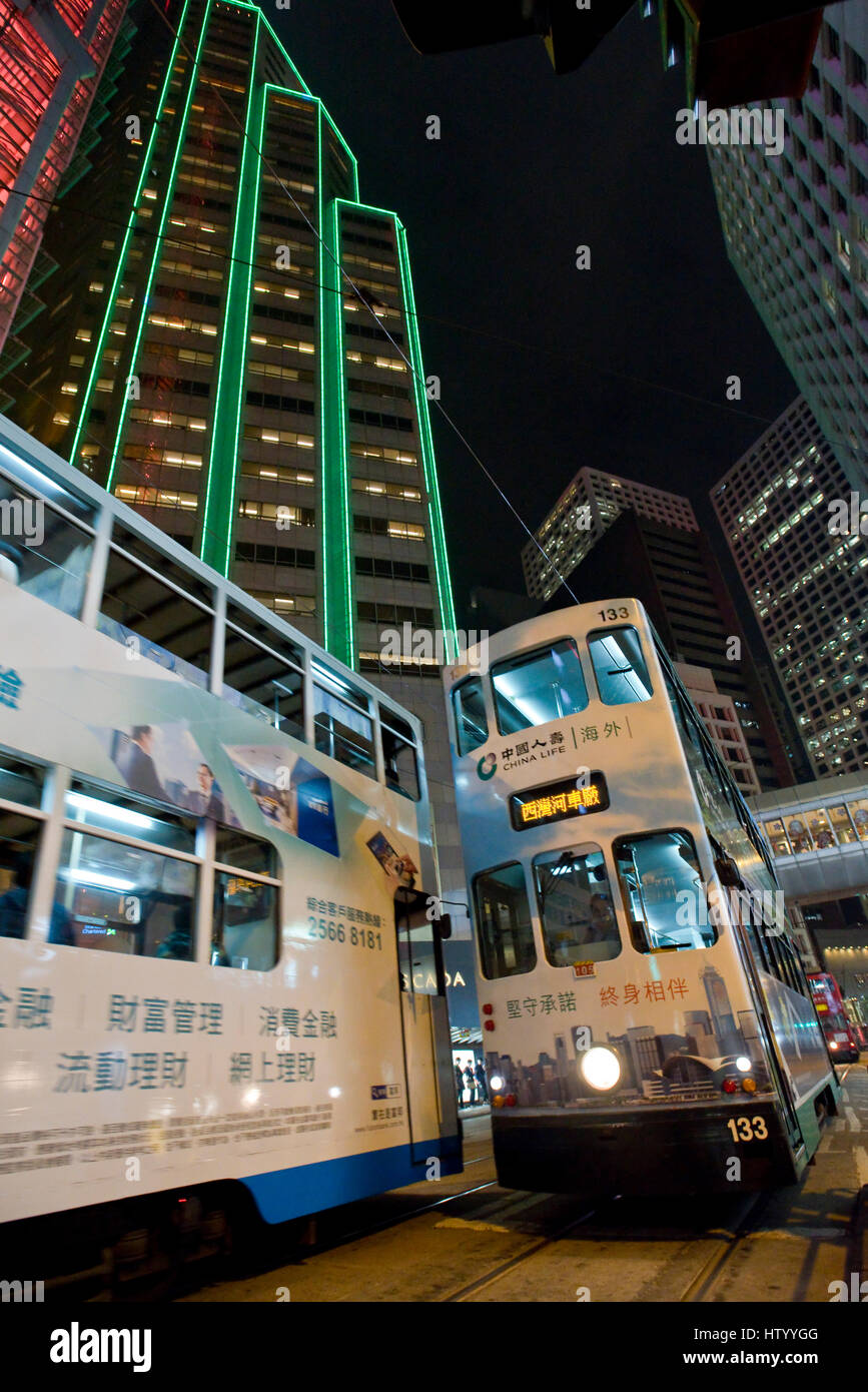 An abstract view of 2 Hong Kong trams meeting travelling along a street in the business district with skyscrapers in the background at night. Stock Photo