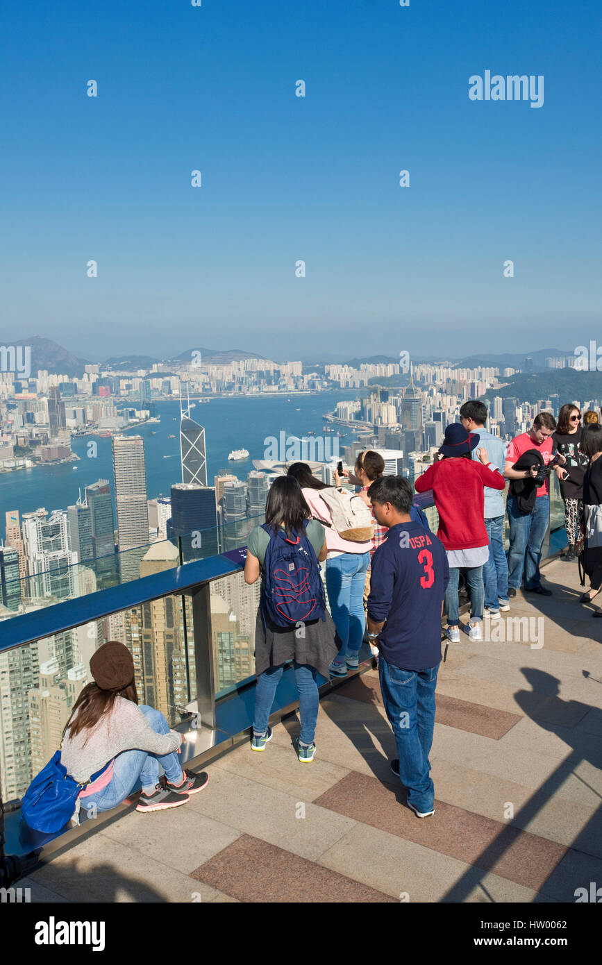 Tourists taking photographs from Sky Terrace 428 on top of the Peak Tower over Hong Kong and Victoria Bay on a clear sunny day with blue sky. Stock Photo