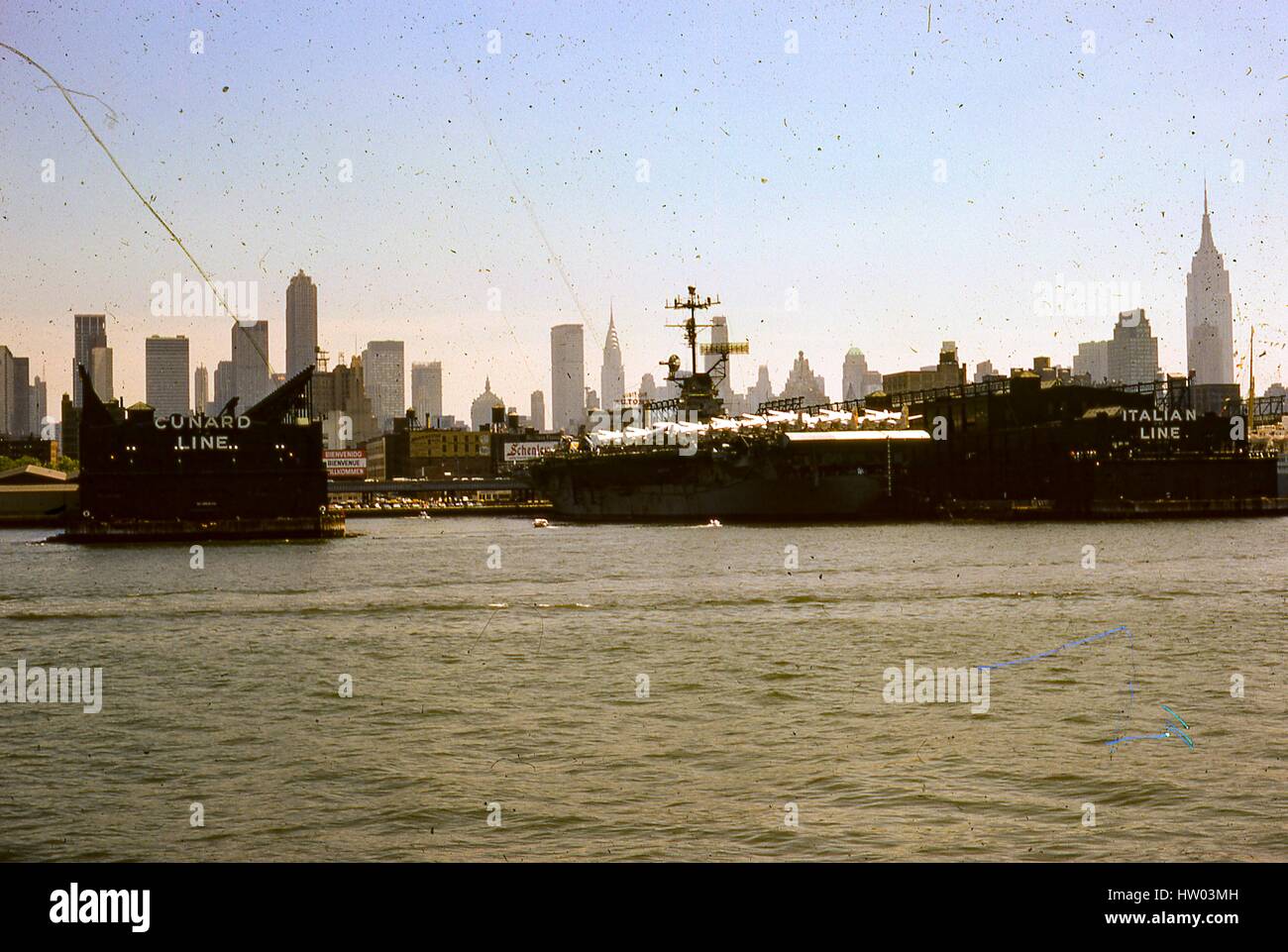 View from the Hudson River of the Cunard Line and Italian Line piers at the New York City Passenger Ship Terminal, known as Luxury Liner Row, in the Hells Kitchen neighborhood on the west side of Manhattan, New York City, New York, August, 1966. Visible in the foreground is a cruise ship docked at Italia's Pier 88, while Cunard is empty at 50th Street's Pier 90. Landmark skyscrapers seen in the background include the GE Building at Rockefeller Center, the Pan Am Building, the Chrysler Building, and the Empire State Building. Stock Photo