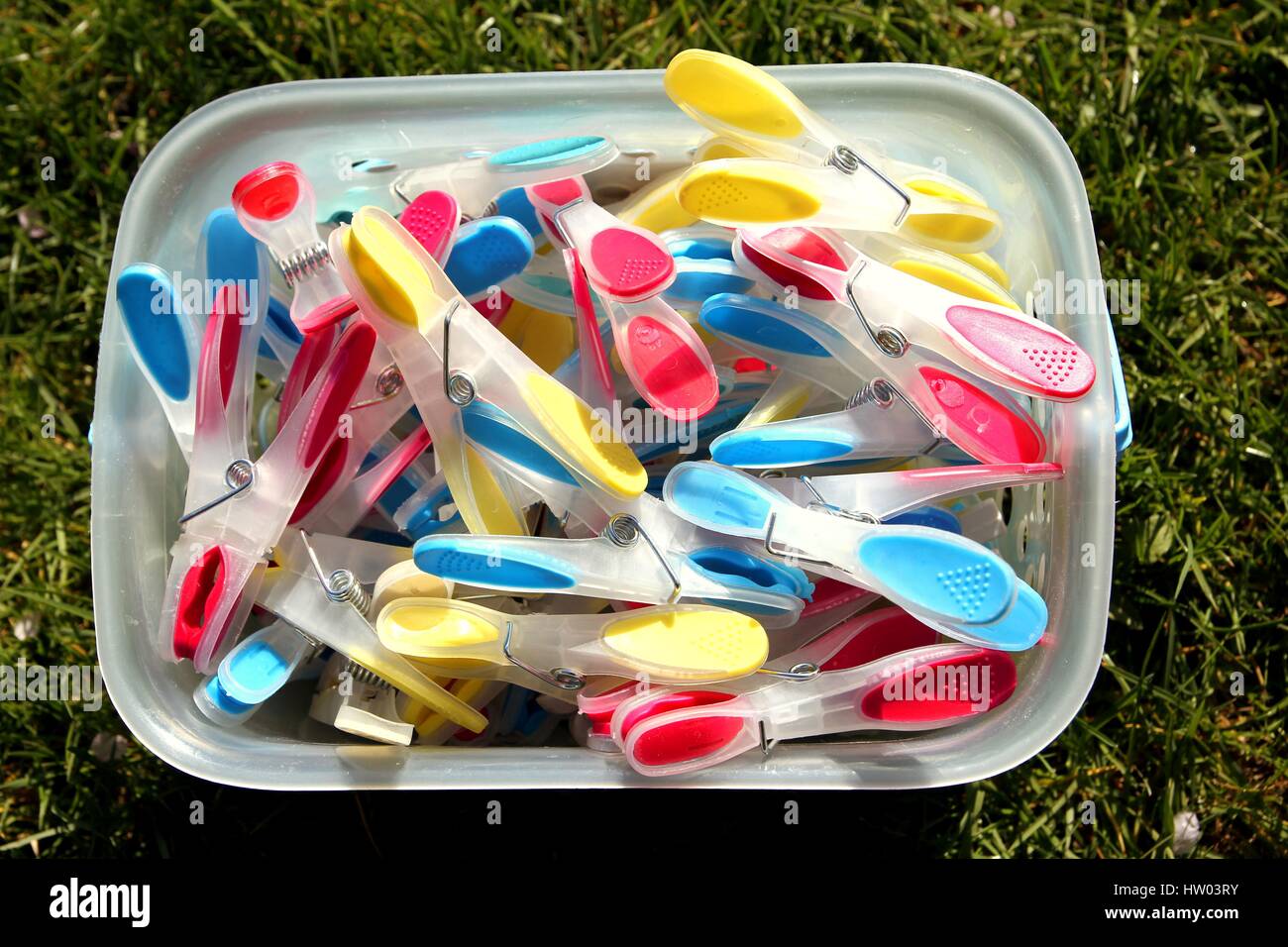 Brightly coloured clothes pegs in a bucket on green grass in sunshine Stock Photo