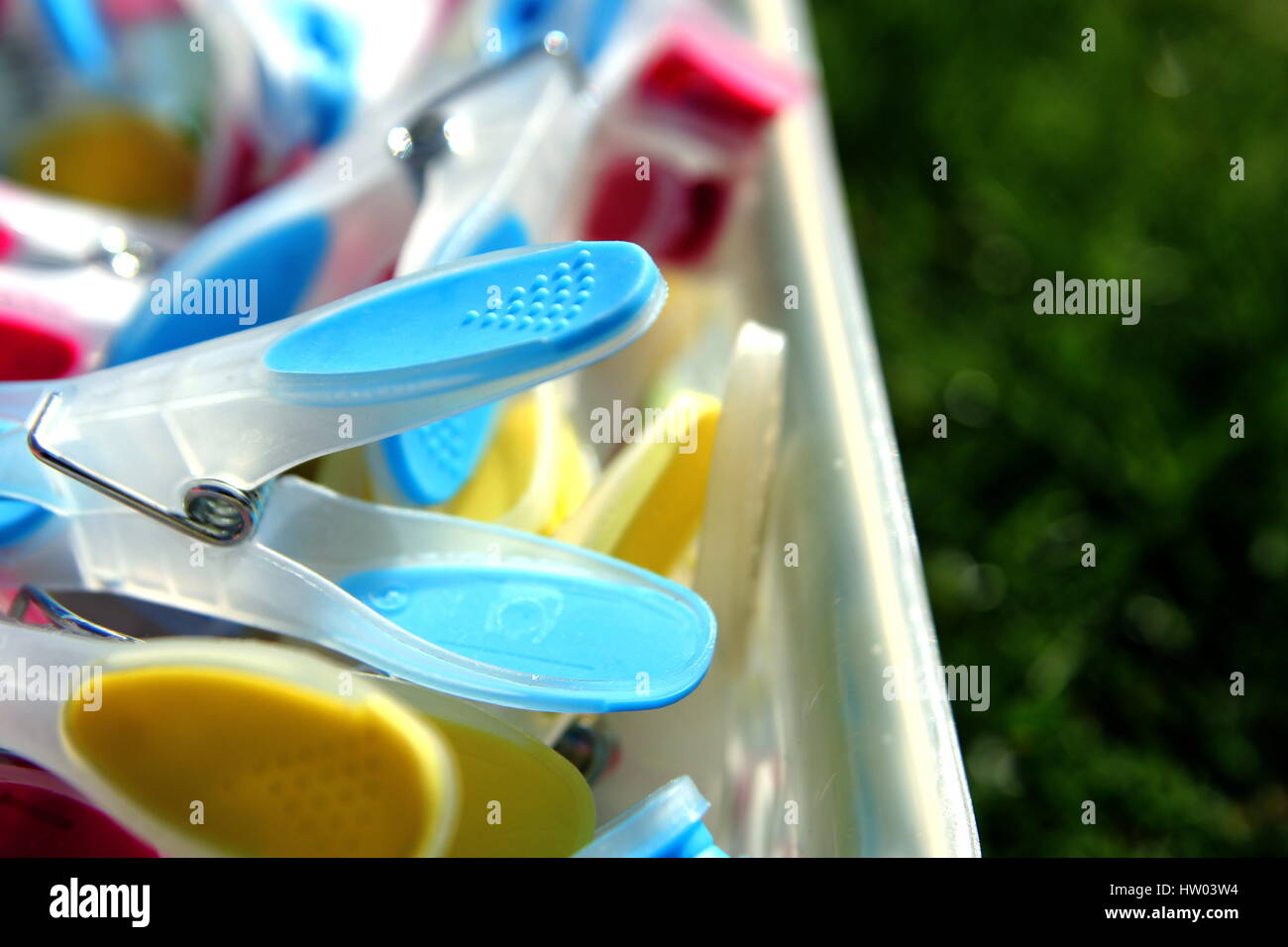 Closeup of brightly colored clothespins in a container on grass, with ...