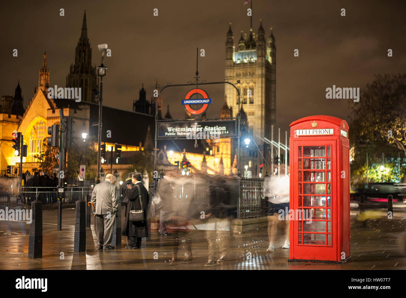 People walking and talking at night near the Westminster underground and the red telephone box in London - UK Stock Photo