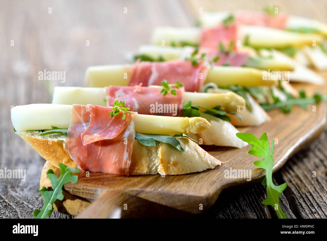 Delicious morsels with white asparagus on rocket leaves wrapped with Italian prosciutto Stock Photo