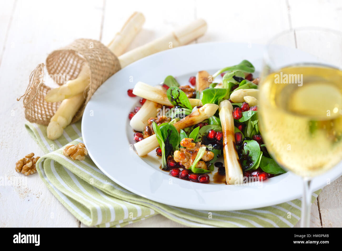 White asparagus on lamb's lettuce with candied walnuts, pomegranate seeds and balsamic vinegar, served with a glass of fruity white wine Stock Photo