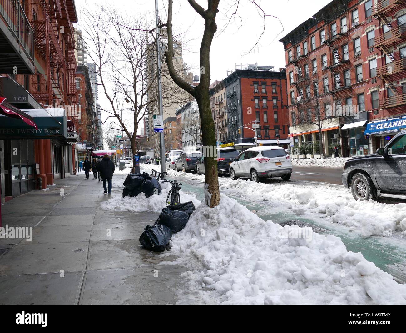 NYC street day after Storm Stella. Pedestrians and cars navigate around garbage, slush and piles of dirty snow. Upper Eastside, New York City, NY, USA Stock Photo