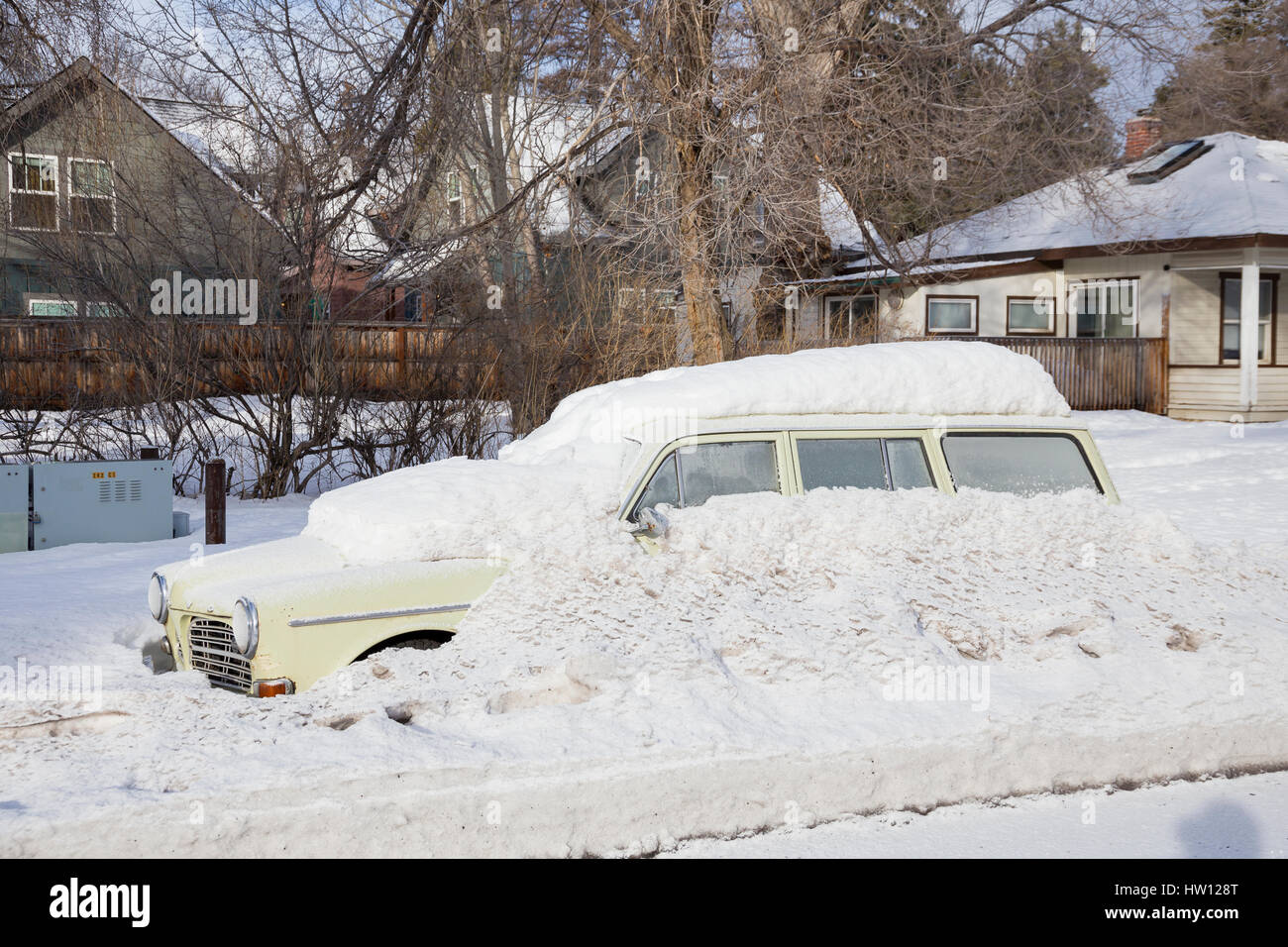 Frozen car underneath a lot of snow is completely stuck on the side of