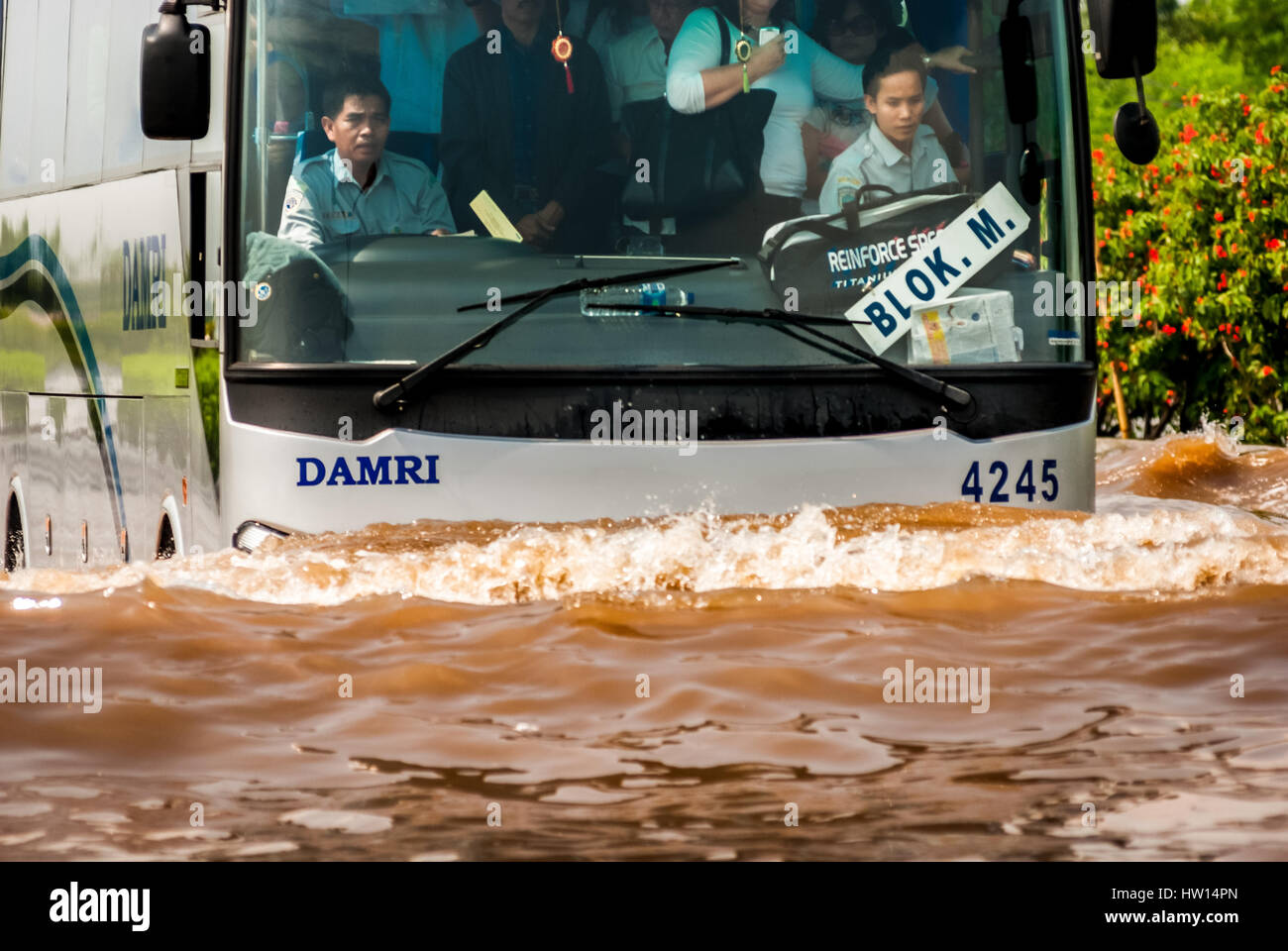 A Jakarta airport shuttle bus packed with passengers makes it way through a flooded street near coastal area. © Reynold Sumayku Stock Photo