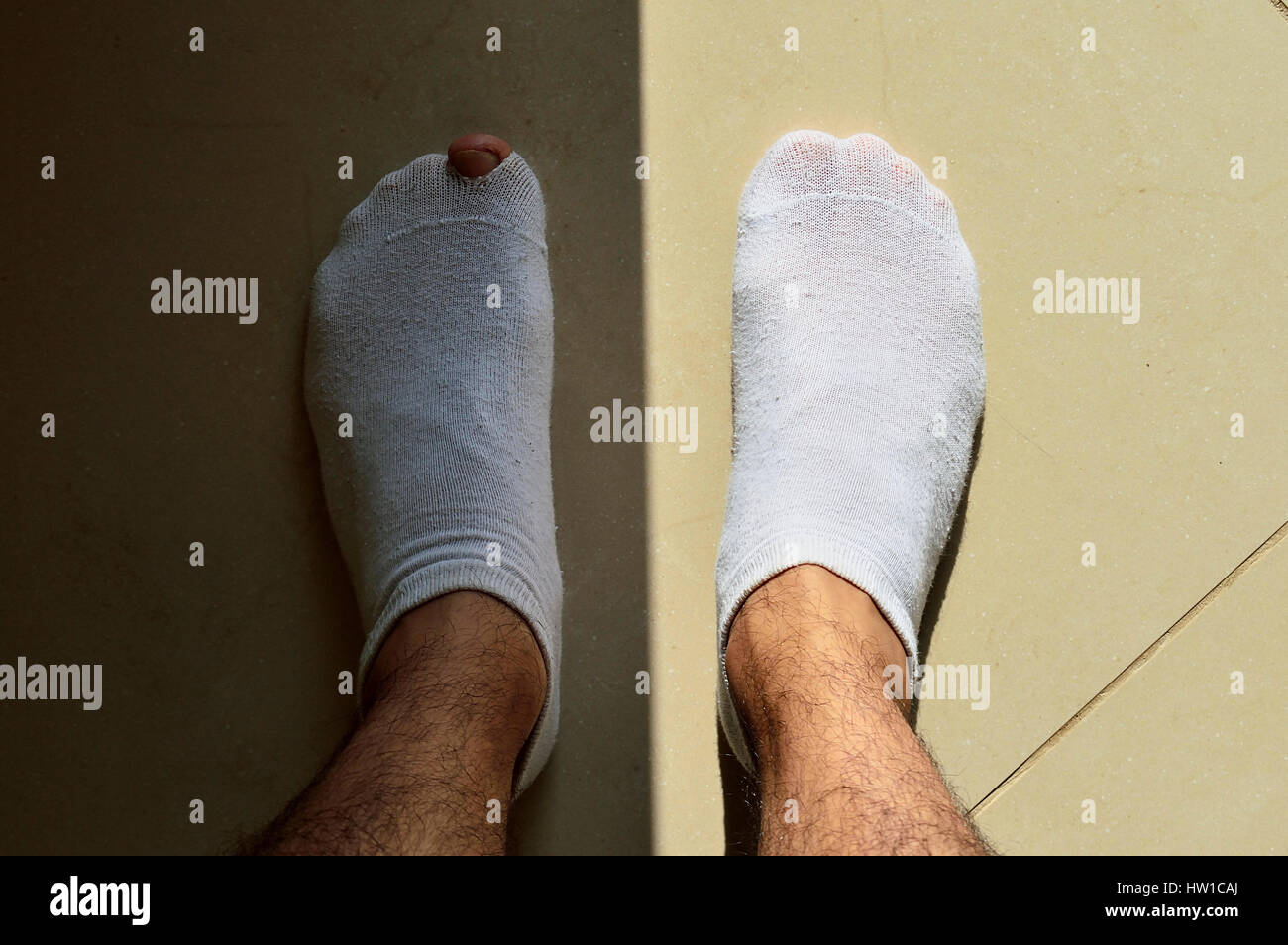 Left foot with a hole in the sock and in the shadow, separated of the right foot by the sun light Stock Photo