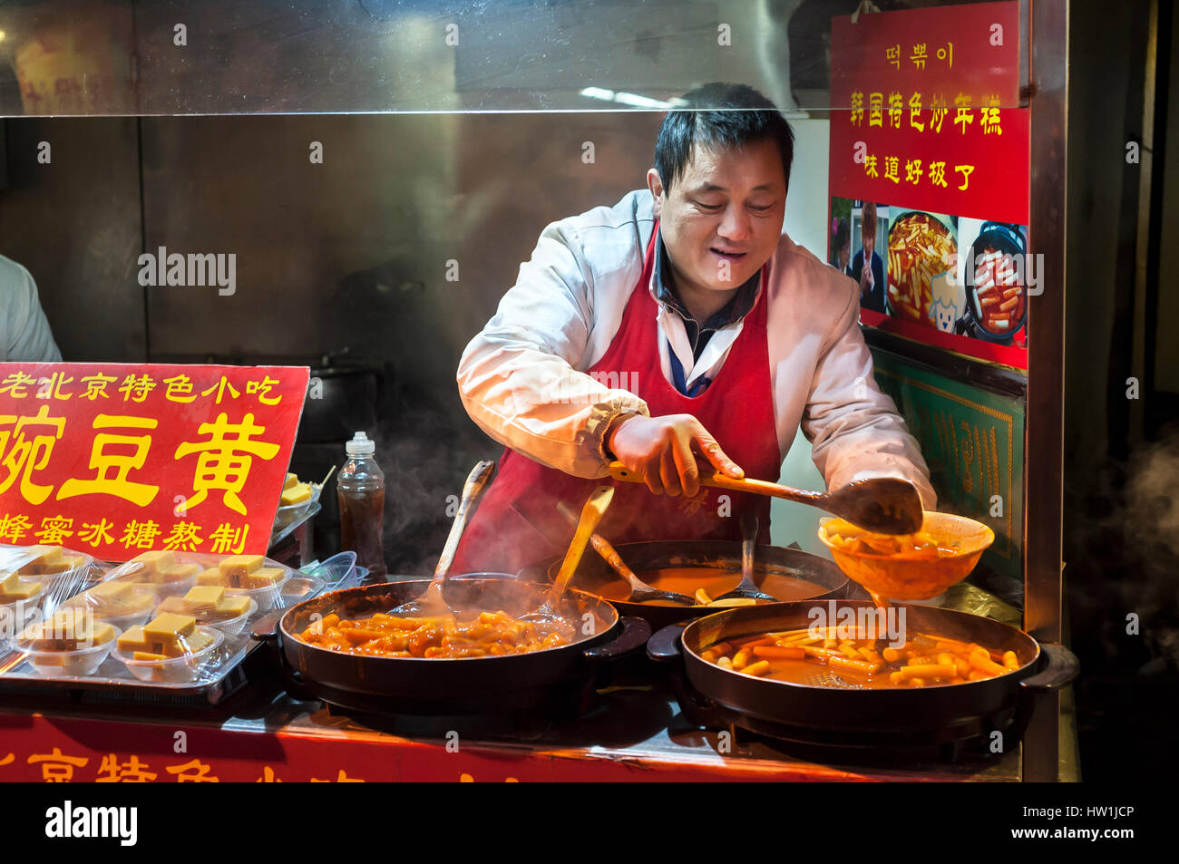 WANGFUJING NIGHT MARKET, BEIJING - DEC 25, 2013 - A vendor serves spicy Korean rice cakes at Wangfujing snack street, Beijing. Stock Photo