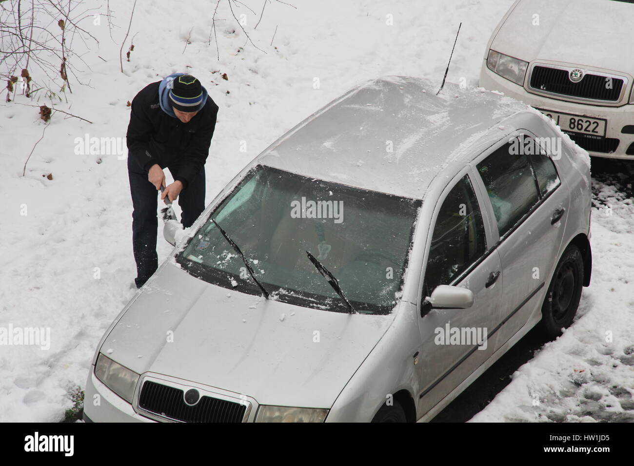 A car owner in Prague's Libeň area scrapes off snow and frost on his vehicle in order to be able to drive off his parked car. Stock Photo