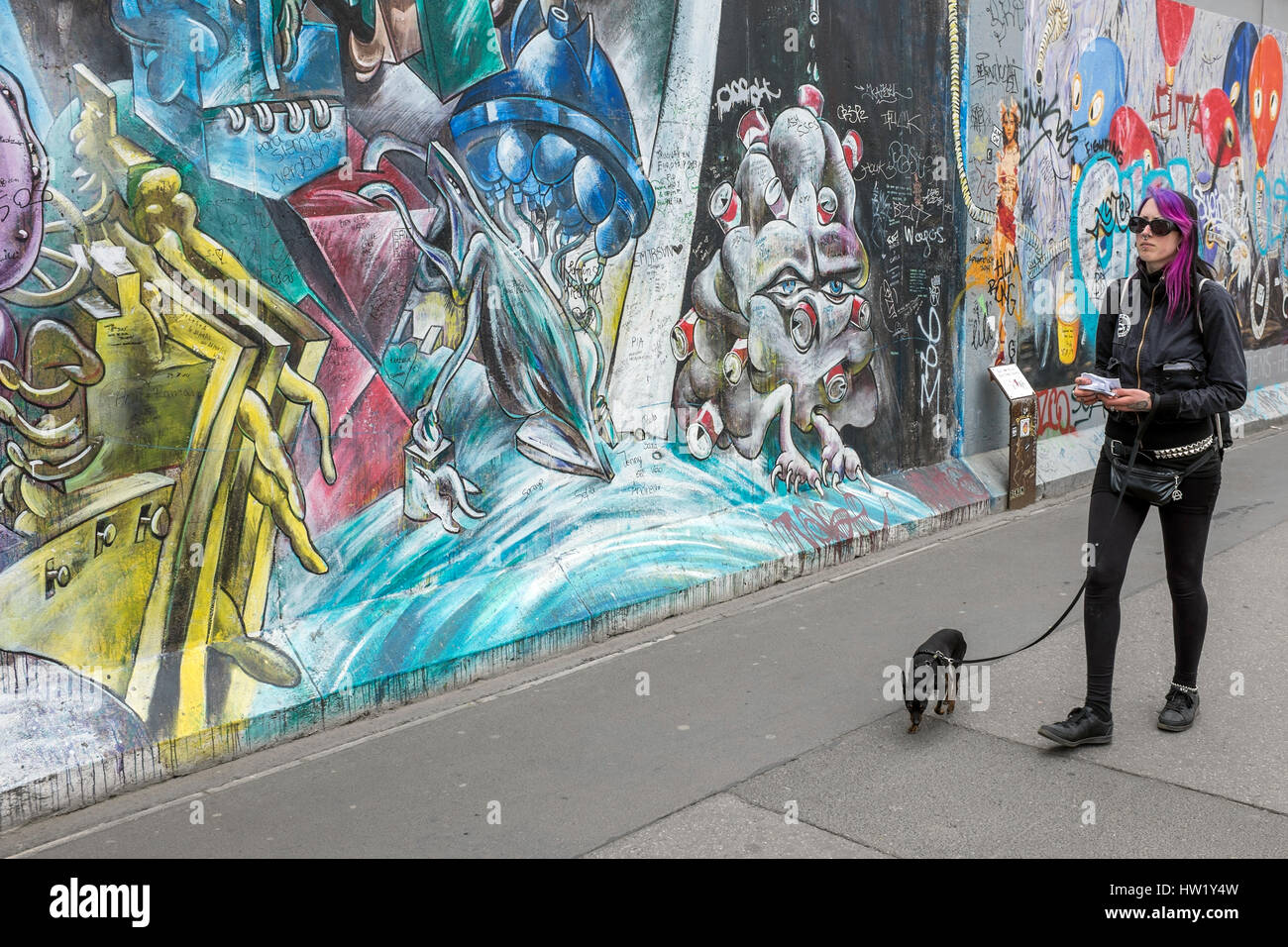 A girl is walking her dog on the East Side Gallery on Mühlenstrasse in Berlin, Germany. The place is an international memorial for freedom in the Frie Stock Photo