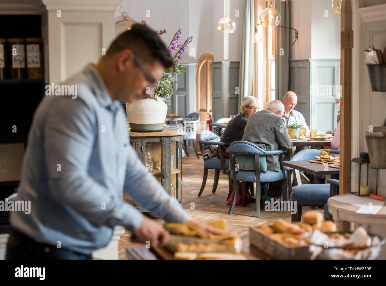 The maitre d’hotel preparing bread while a group of retired people have lunch at The Painswick, near Stroud, Gloucestershire UK Stock Photo