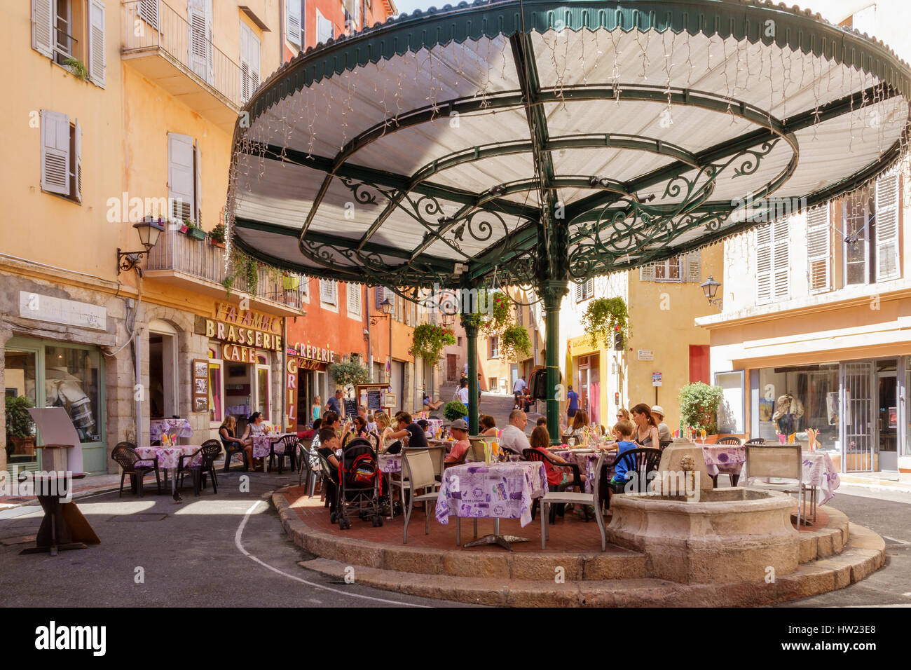 Families dining al-fresco under an ornate glass canopy in a historic square in Grasse, Provence, in the French Alps. Stock Photo