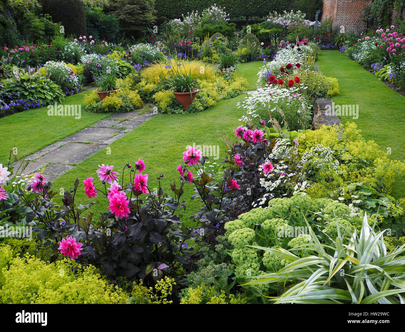 Chenies Manor Sunken garden in late July with lawn, path and vibrantly coloured pink dahlias, shades of green foliage and ornamental pond facing west. Stock Photo