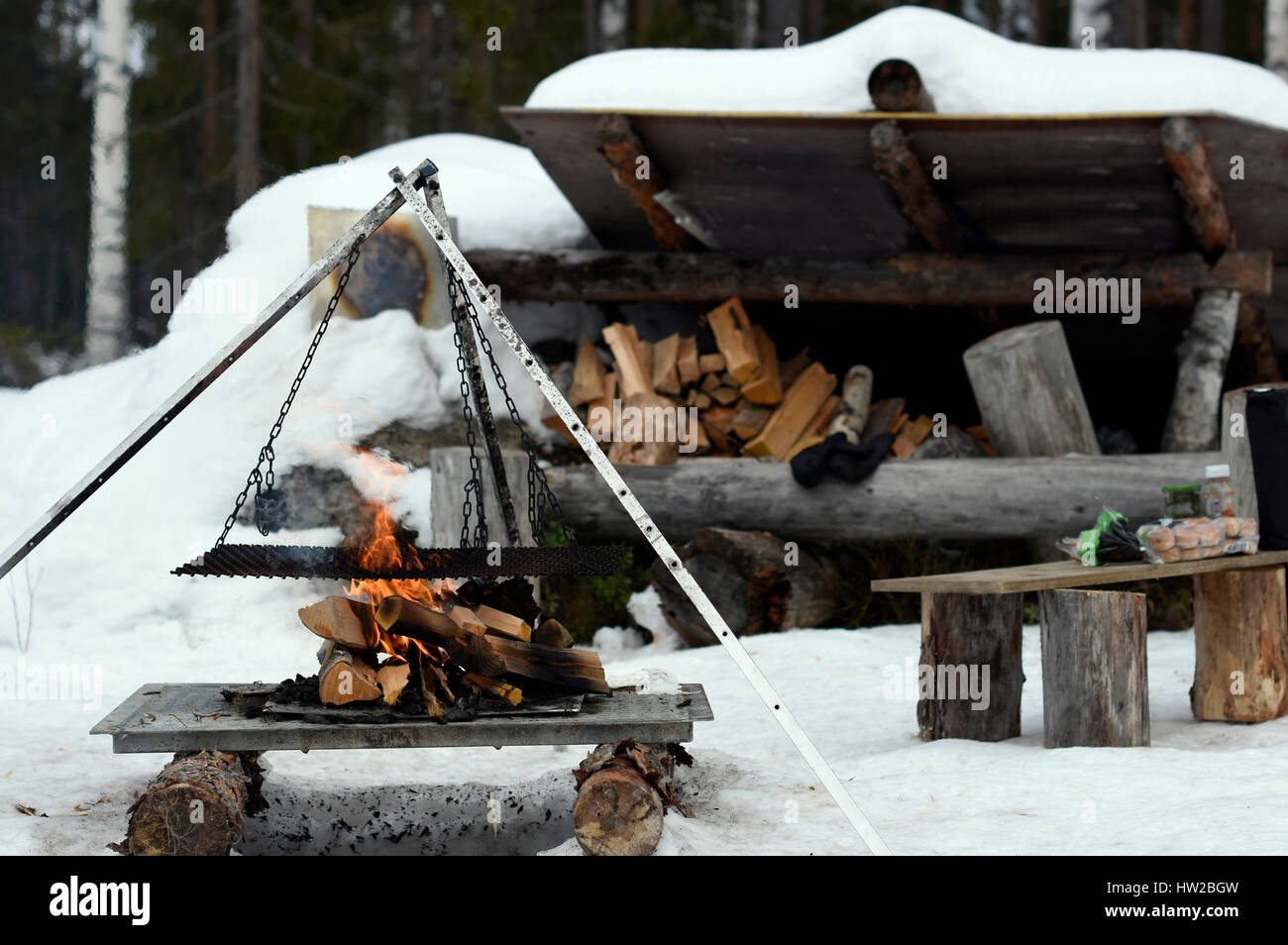 Construction for cooking in nature in winter on a burning fire and a hiking shelter in background picture from the North of Swedn. Stock Photo