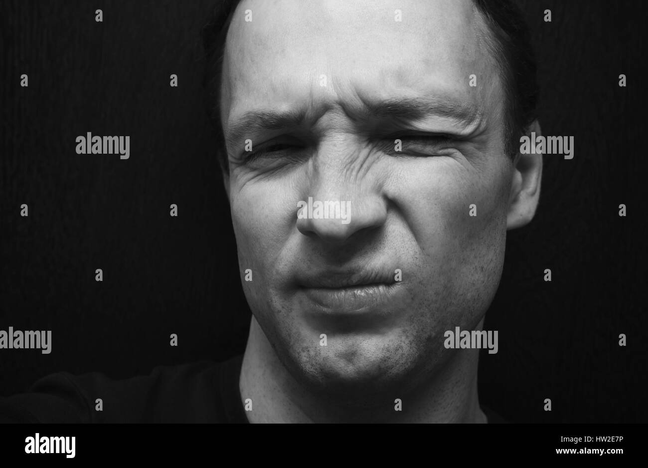 Young confused Caucasian man. Close-up studio face portrait over dark wooden wall background, selective focus, black and white photo Stock Photo