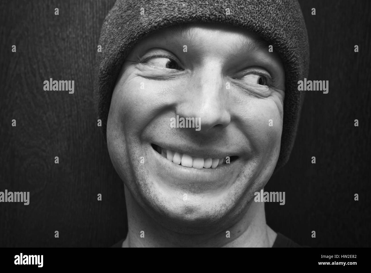 Young handsome smiling man in gray hat. Close-up studio face portrait over dark wooden wall background, selective focus, black and white photo Stock Photo