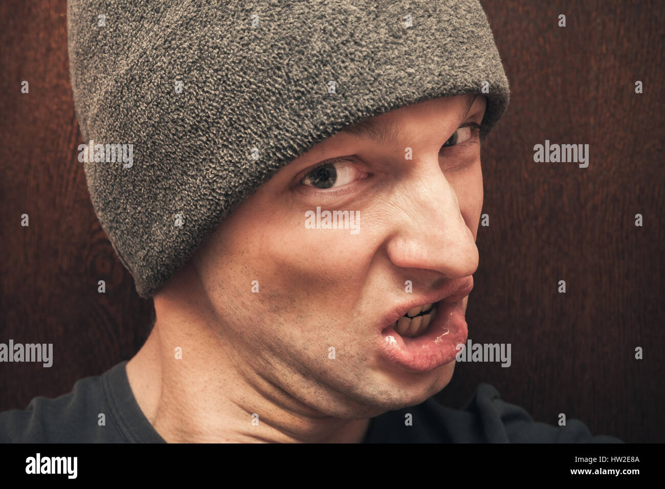 Young agressive Caucasian man in gray hat. Closeup studio face portrait on dark wooden wall background, selective focus Stock Photo
