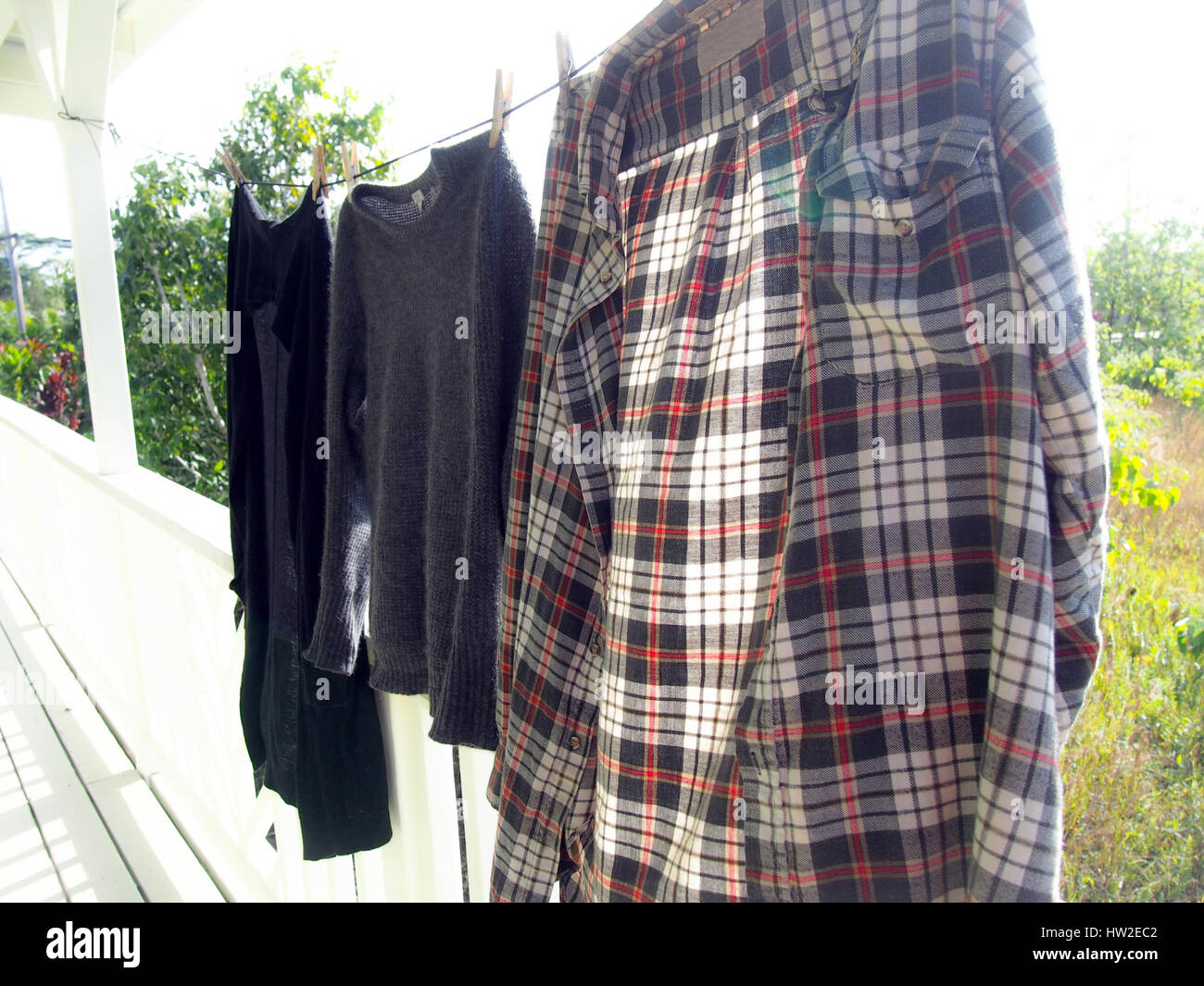 A flannel shirt and two other sweaters hanging on a clothesline in the sun. Stock Photo