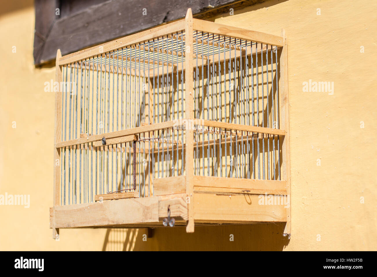 empty wooden birdcage hanging on yellow  wall Stock Photo