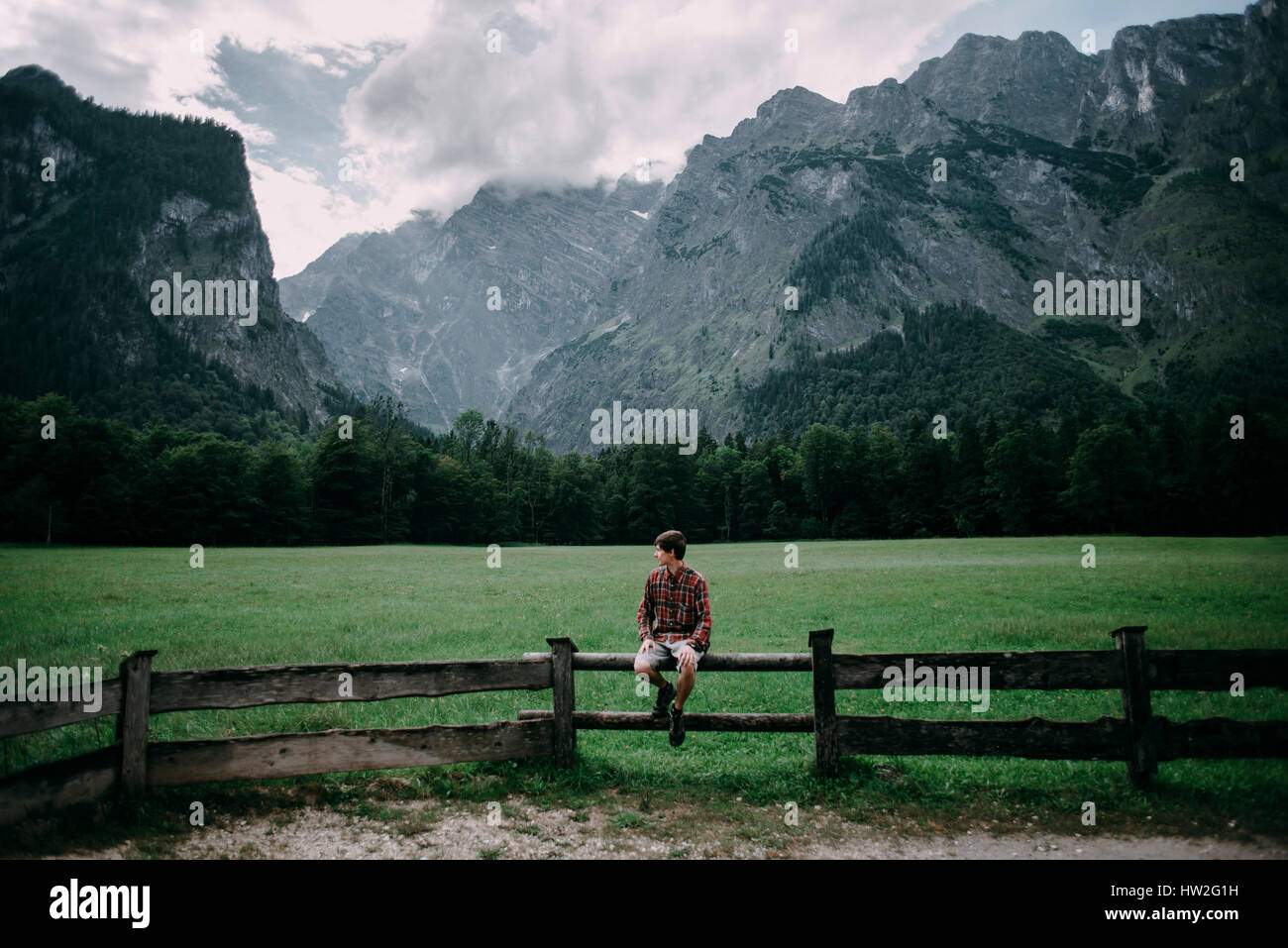 Caucasian man sitting on wooden fence near mountains Stock Photo