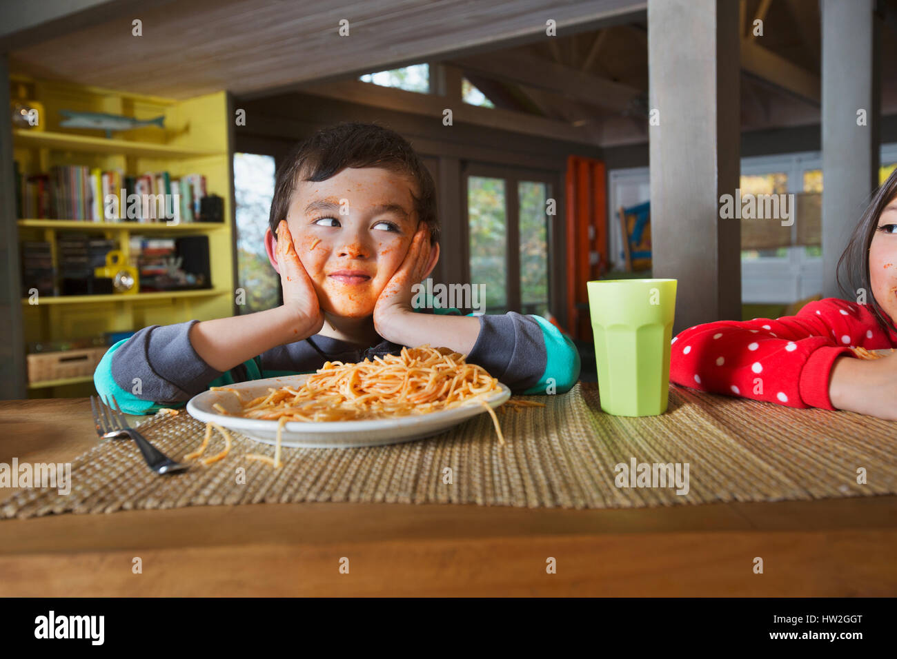 Sister watching Mixed Race brother with messy face eating spaghetti Stock Photo