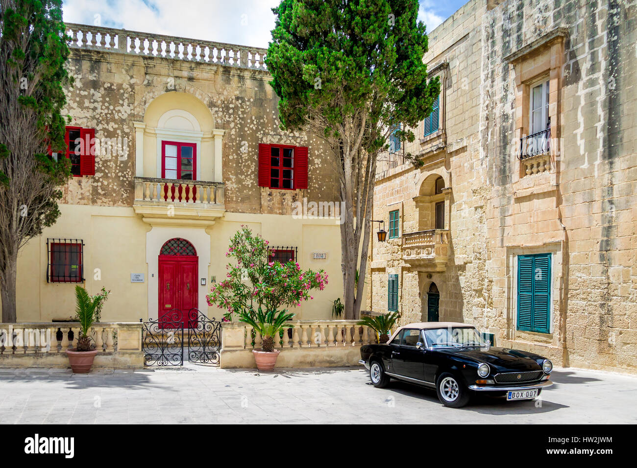 Old stone house with colorful windows and black classic style convertible car - Mdina, Malta Stock Photo