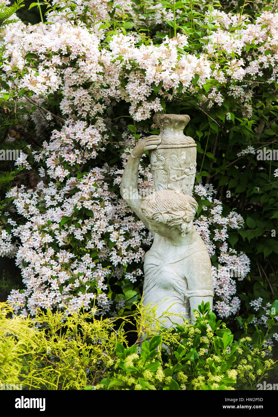 Garden statue constructed out of cement, amongst the flowers of a beauty bush. Stock Photo