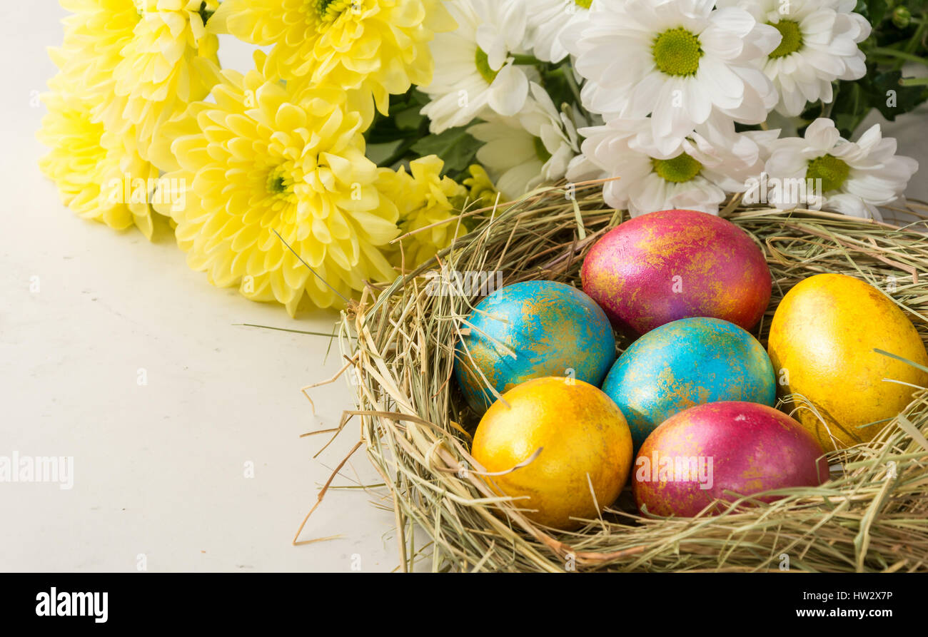 Easter eggs in a straw nest, Easter bunny cookies , yellow and white flowers lie on the background of a white table Stock Photo