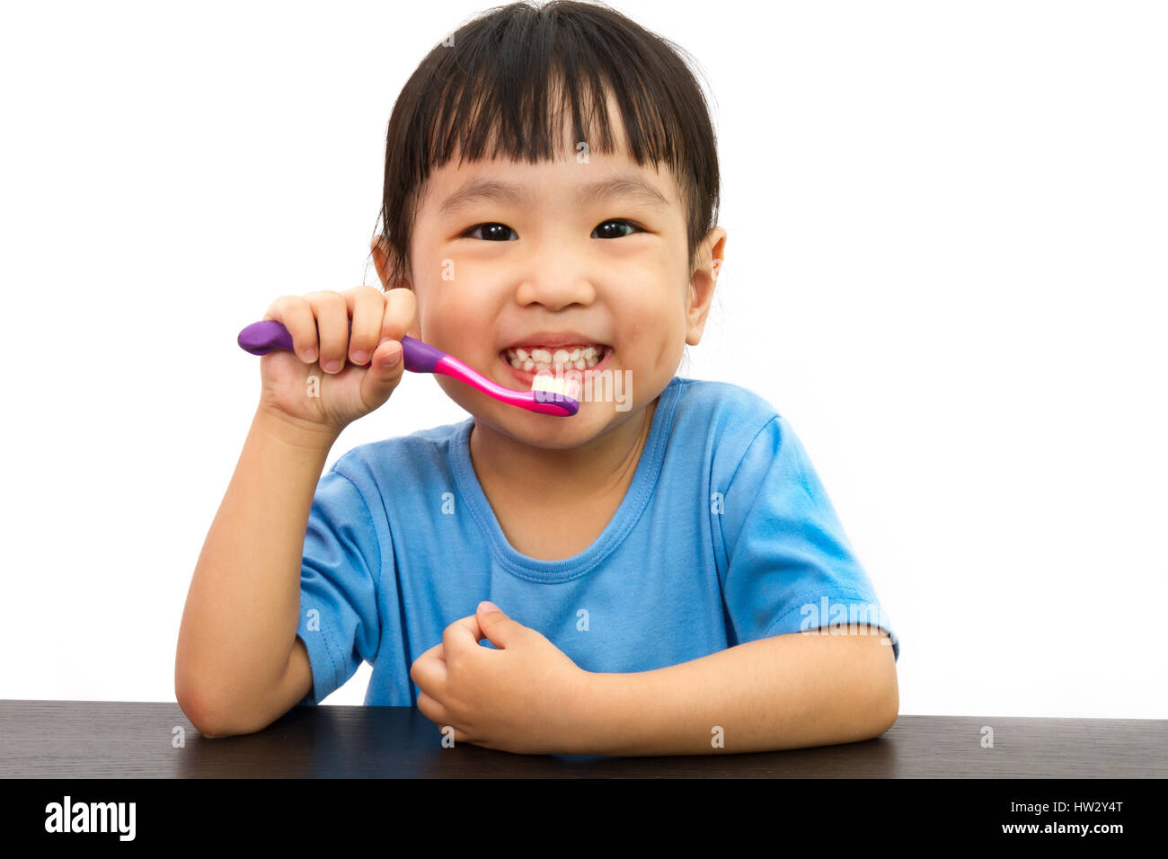 Chinese little girl brushing teeth in plain white isolated background. Stock Photo