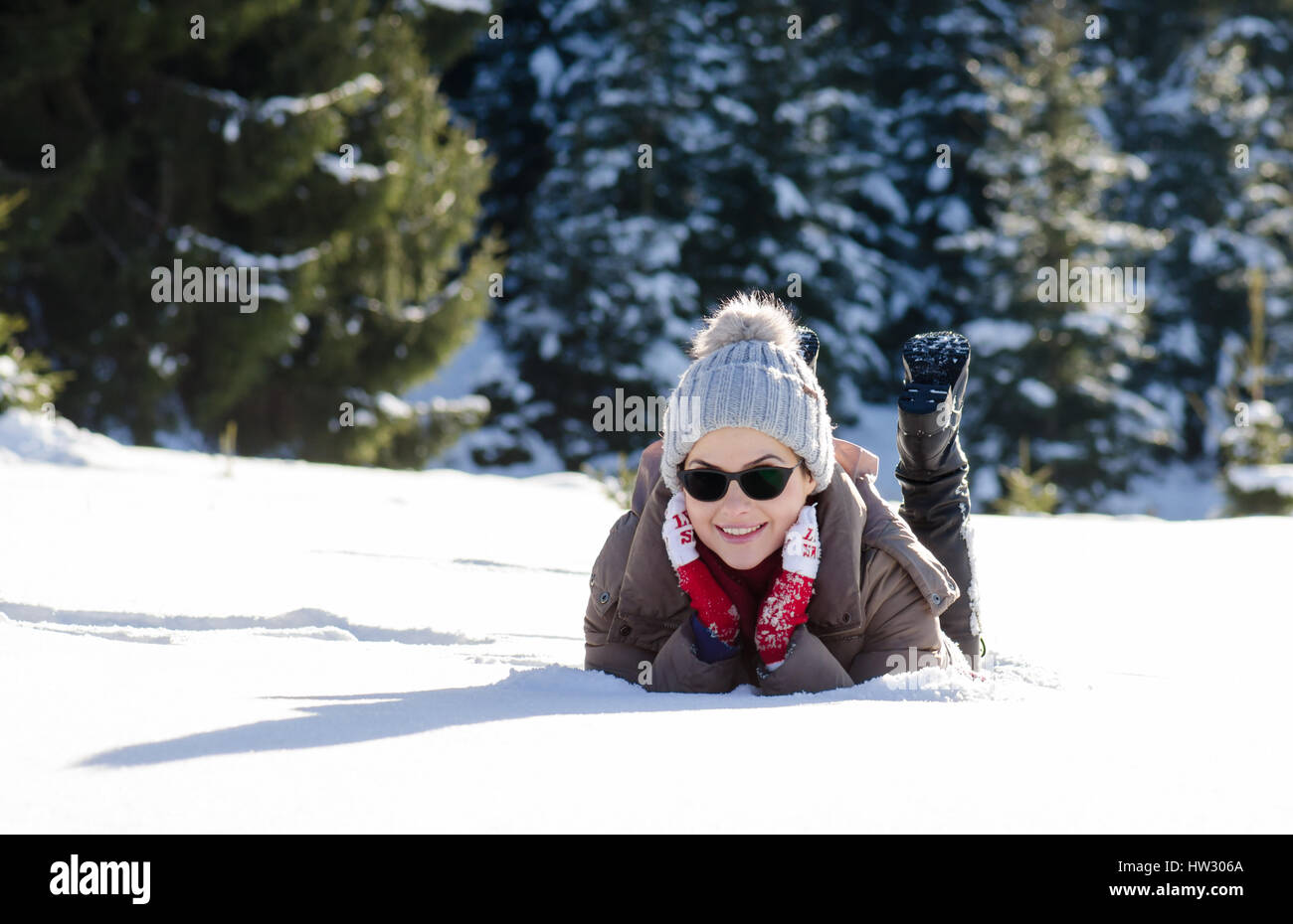 Happy woman having fun in snow lay with red wool gloves and sunglasses Stock Photo