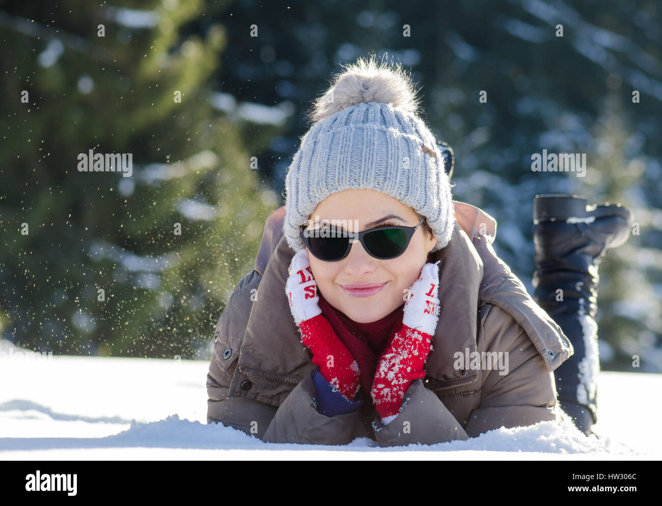 Happy woman having fun in snow lay with red wool gloves and sunglasses while snowing Stock Photo