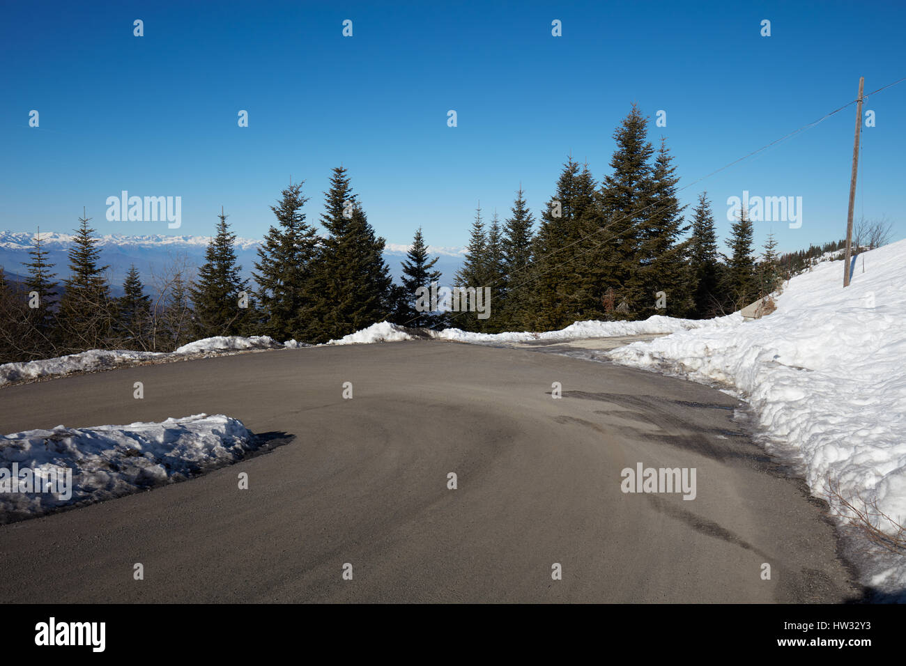 Empty mountain road curve on Alps with pine trees and snow on sides Stock Photo