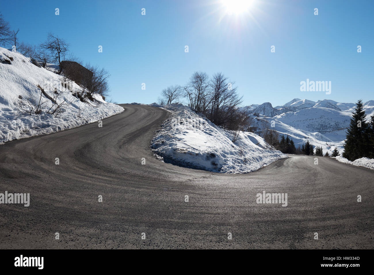 Empty mountain road curve on Alps with snow on sides, blue sky in a sunny day Stock Photo