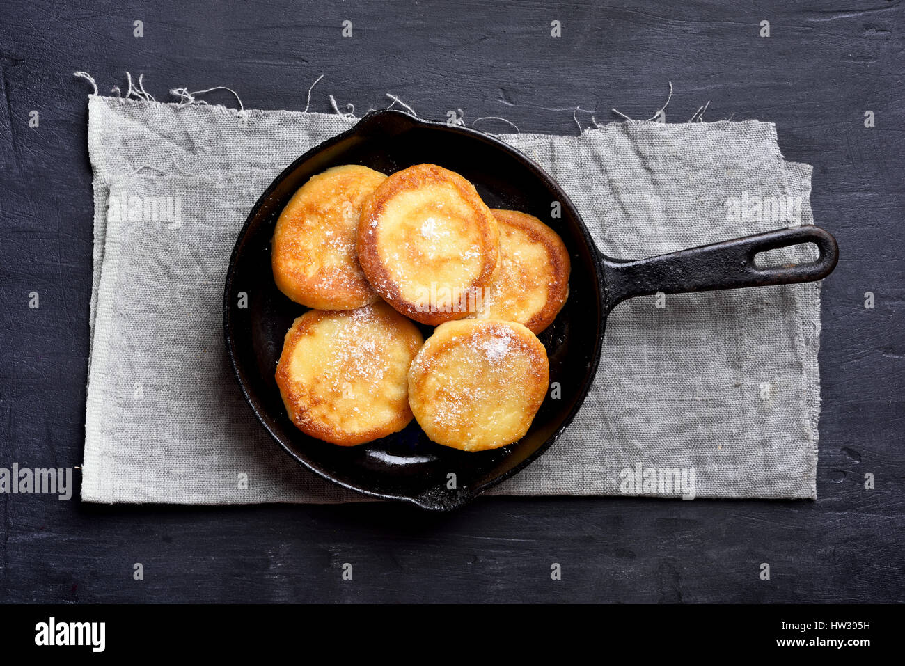 Cheese pancakes, cheesecakes in frying pan on dark background, top view Stock Photo