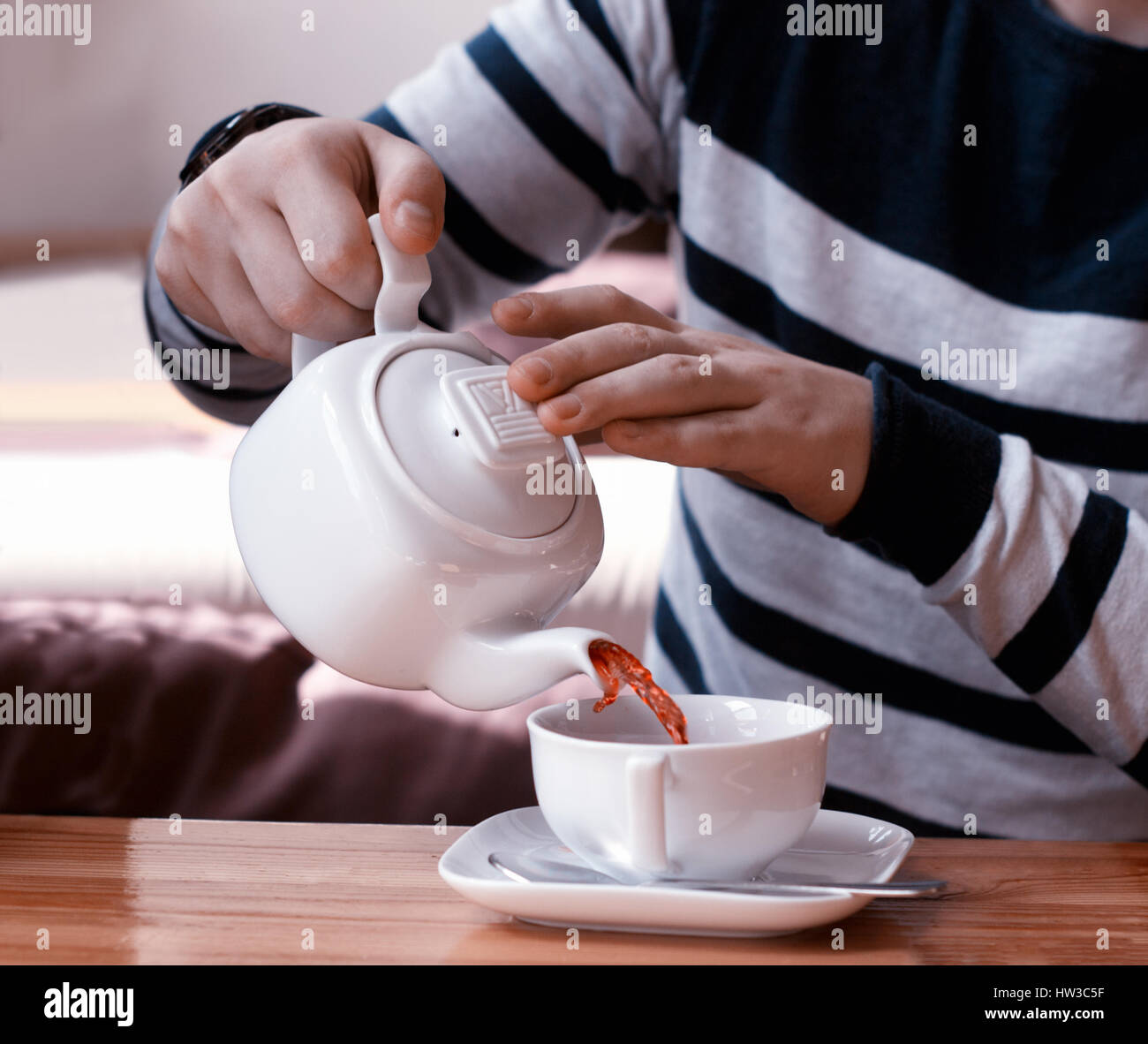 man pours fruit tea from teapot into the white cup on wood table Stock