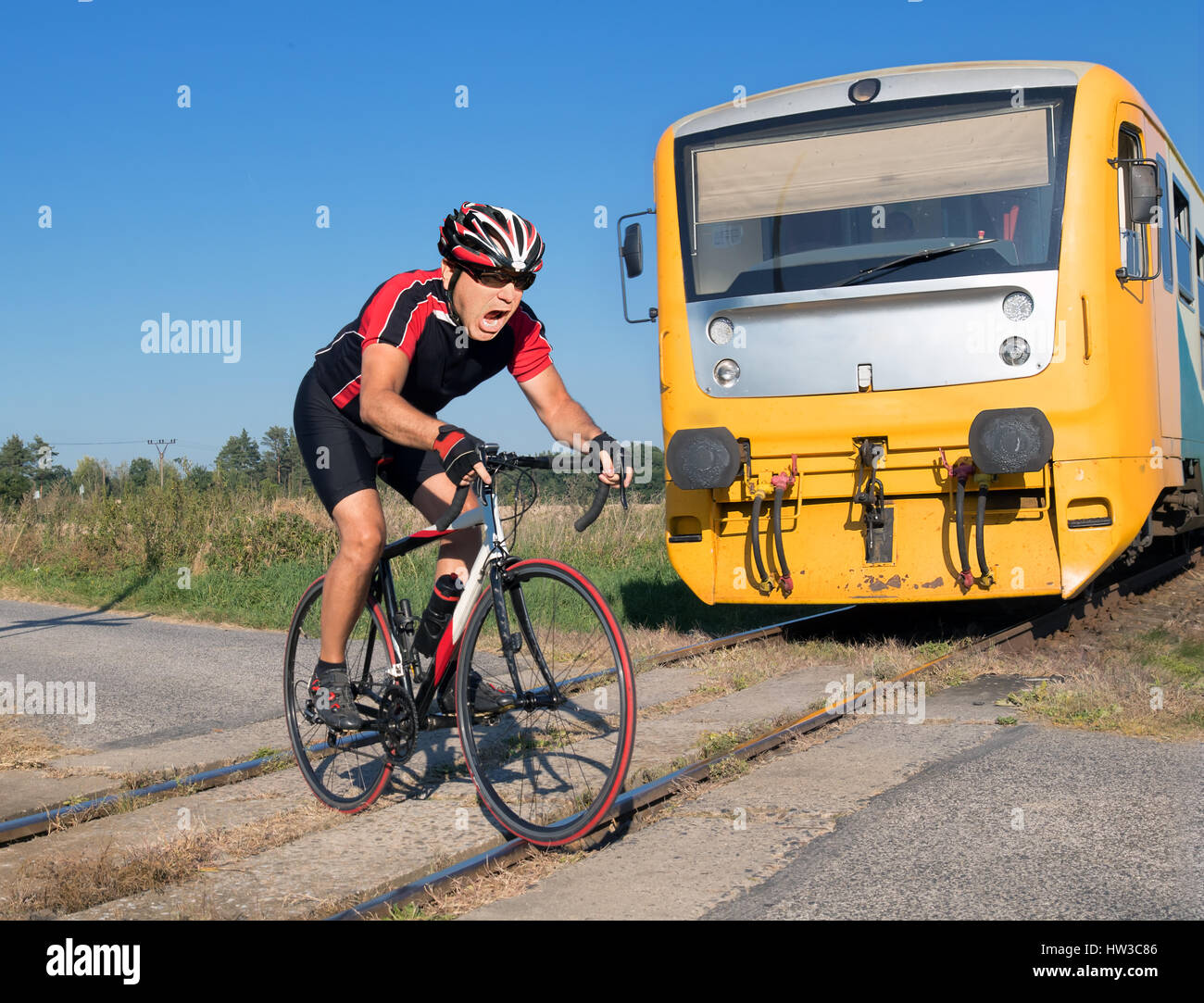 Terrified cyclist is rushing before by train on the tracks. Shocked biker ride a railway crossing in front of an approaching train. The regional train Stock Photo
